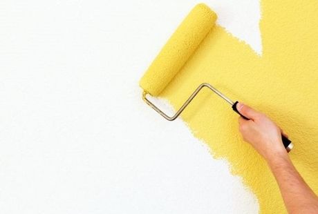 Picture of a painter rolling a paint brush on a wall with yellow paint.