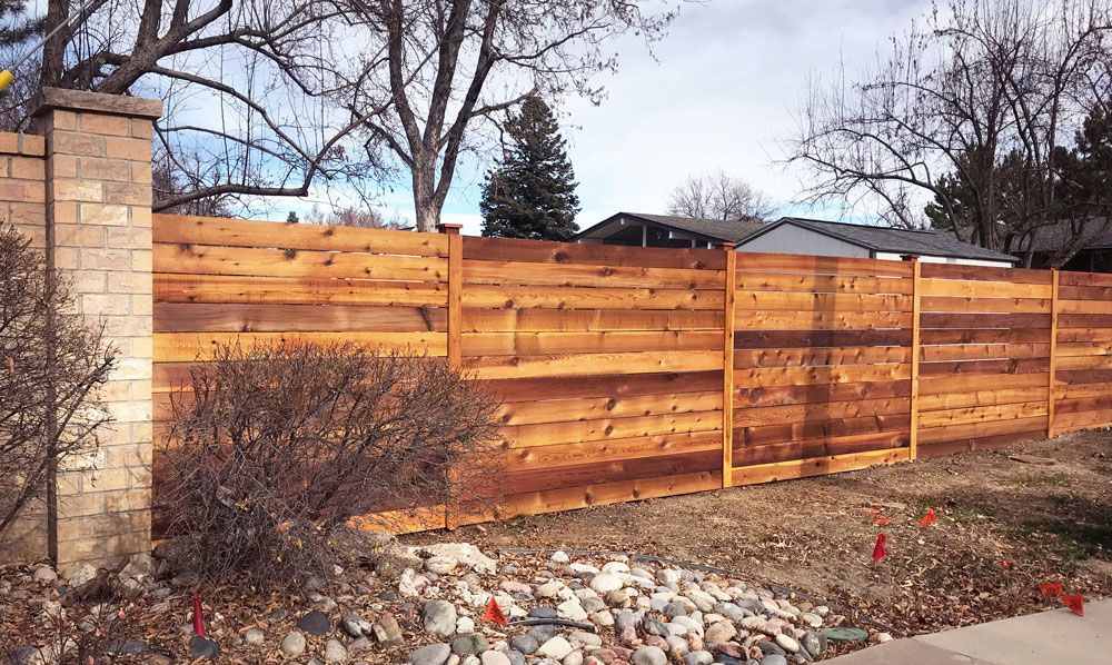 A wooden fence is sitting next to a brick wall in front of a house.