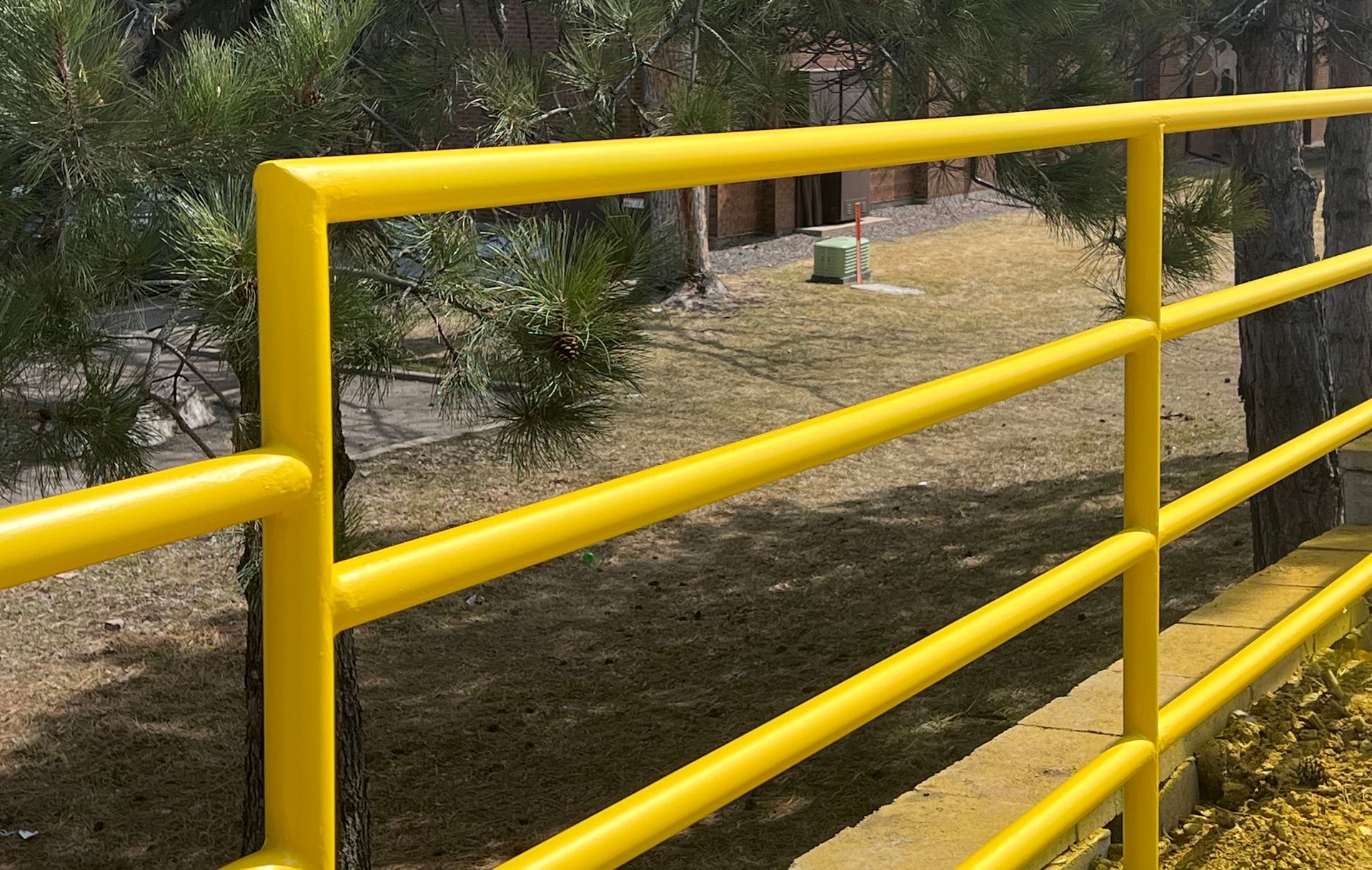 A yellow metal fence with trees in the background.