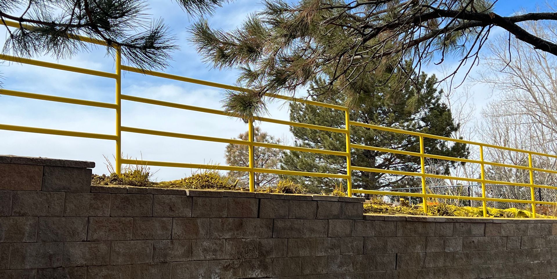 A yellow railing on a brick wall with trees in the background