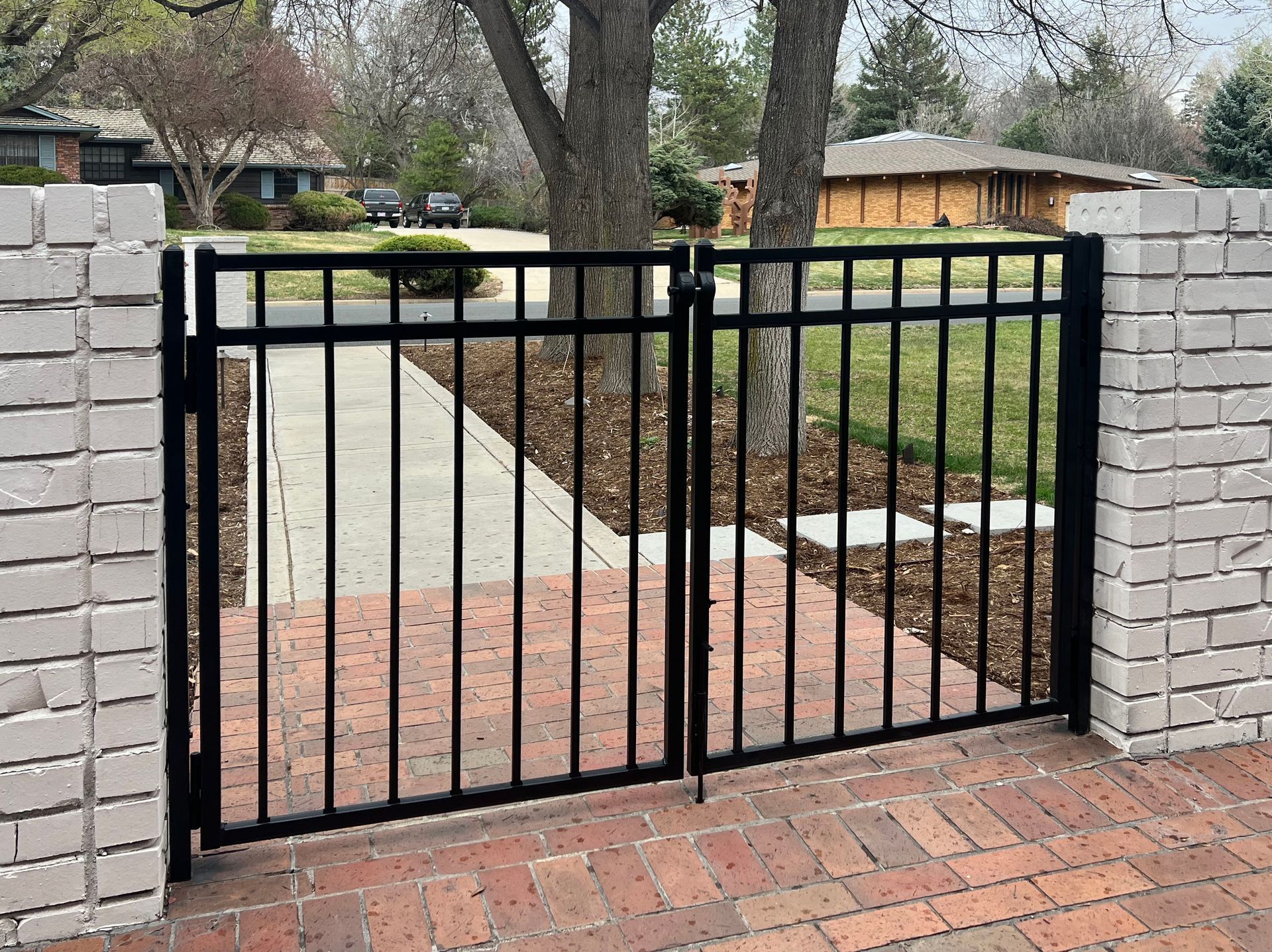 A black gate is sitting on a brick walkway in front of a house.