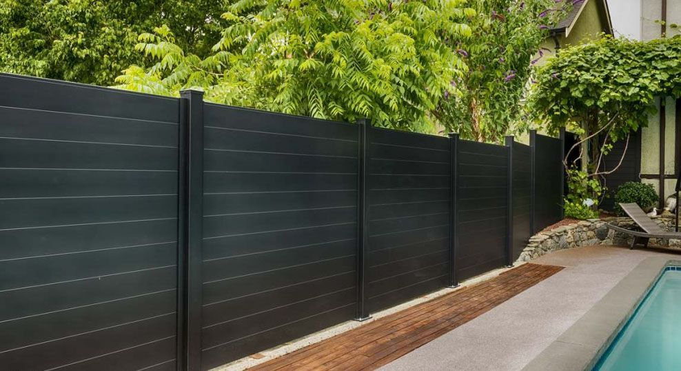 A black fence surrounds a swimming pool in a backyard.