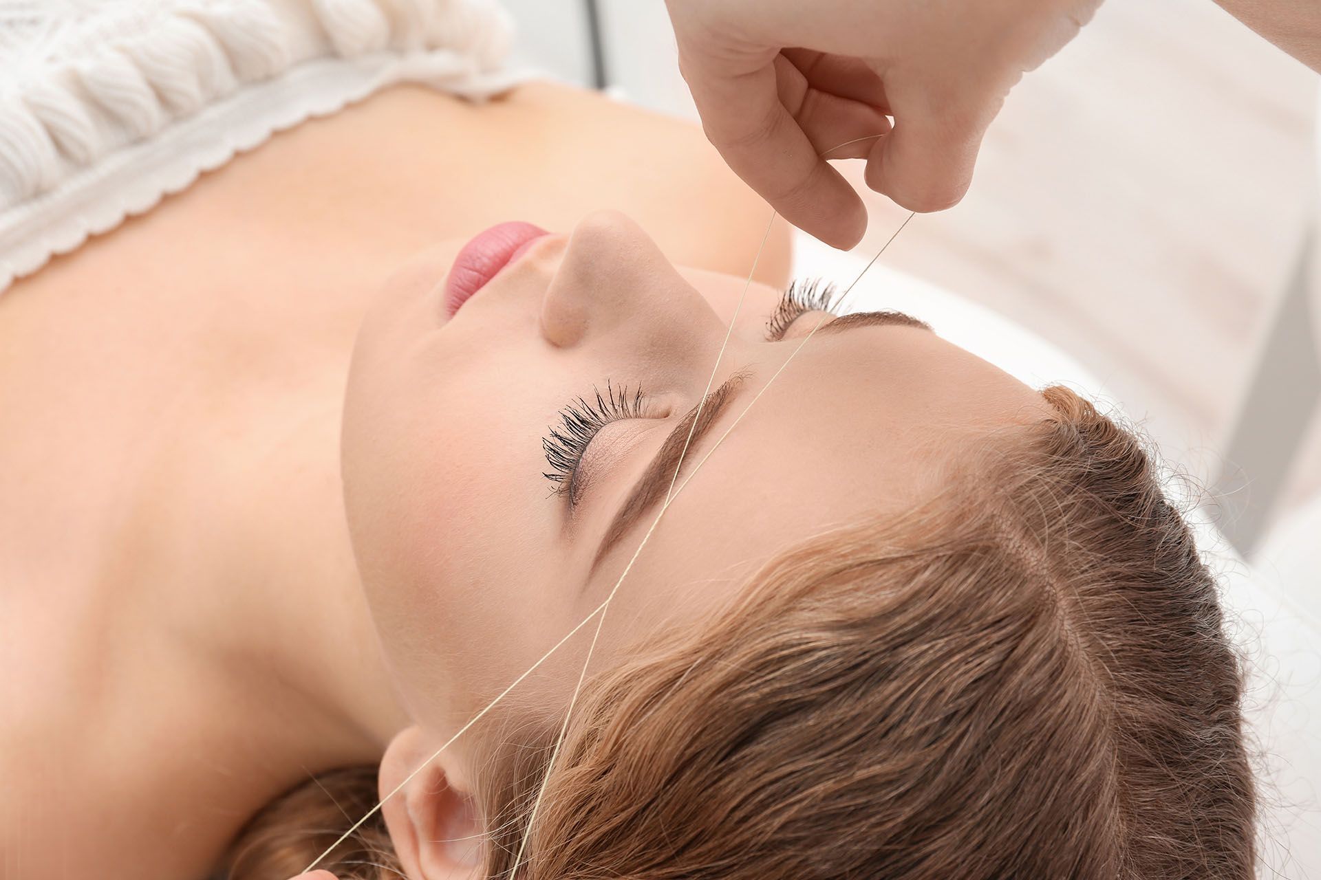 Woman getting eyebrow threading done at a salon.