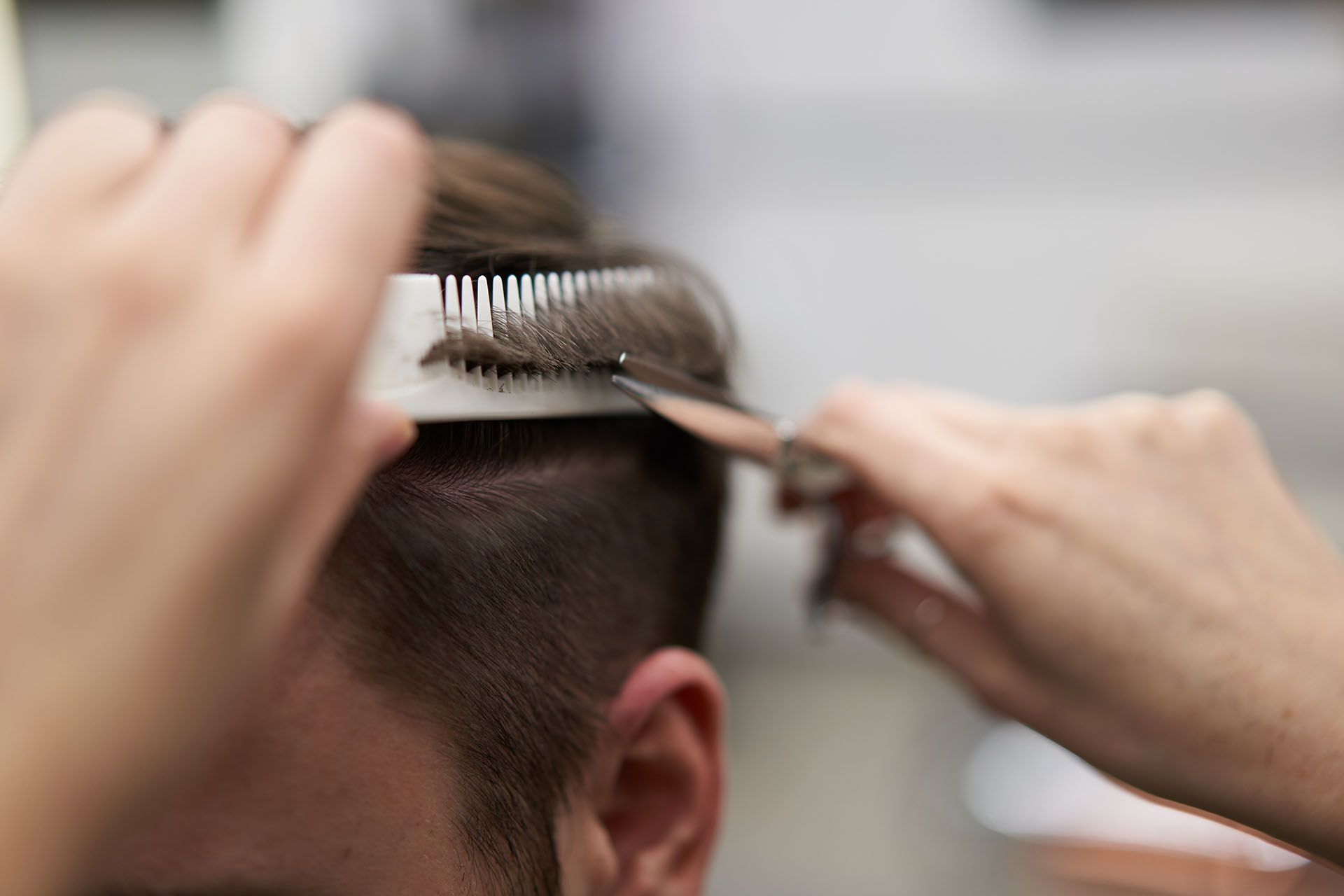 Hairdresser cutting a man's hair with comb and scissors. Close-up shows hair, comb, scissors, and hands.