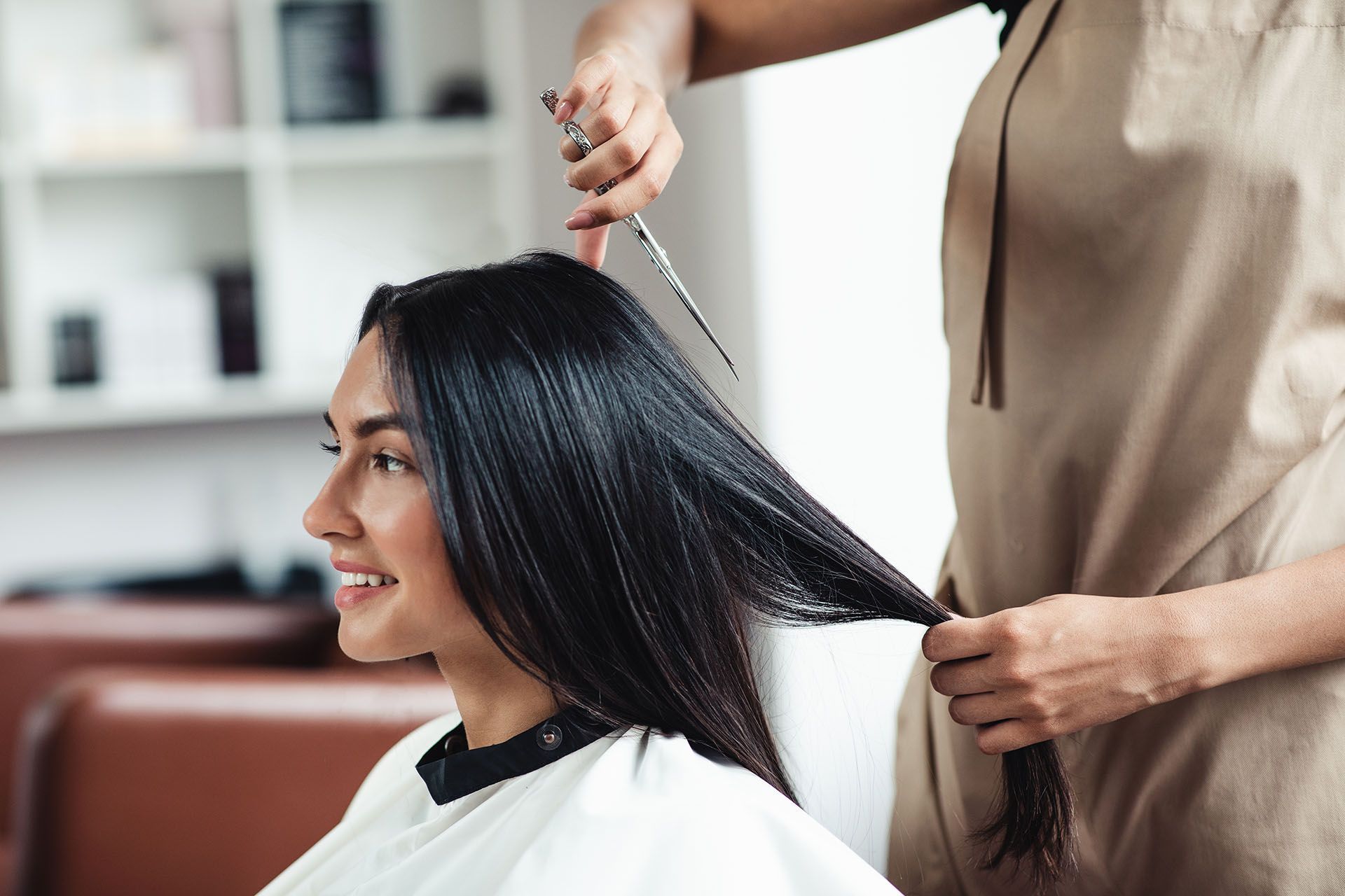 Woman getting her hair cut at a salon. Smiling, dark hair. Hairdresser holding scissors, tan apron.