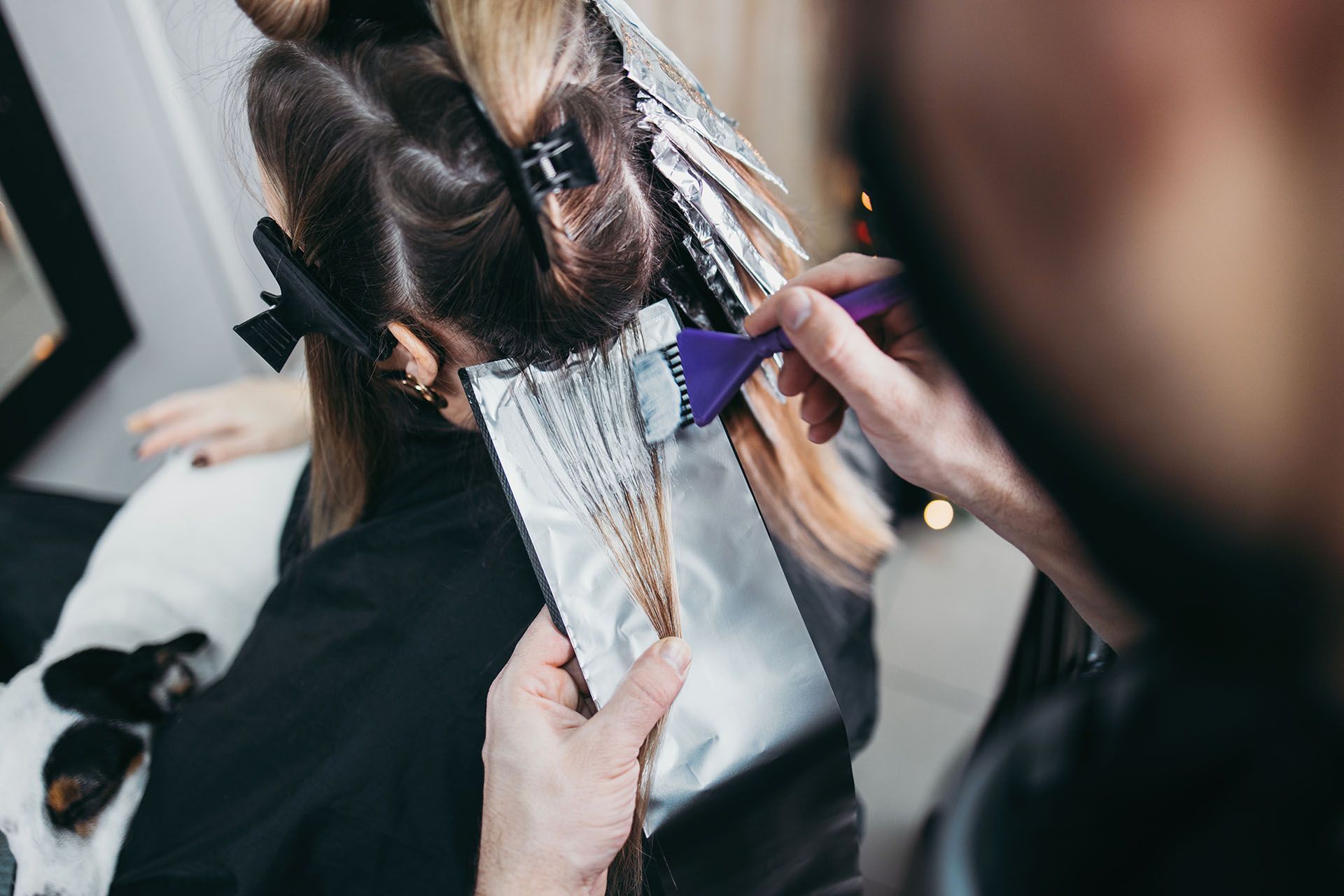 Hairdresser applying bleach to client's hair using a brush and foil in a salon.