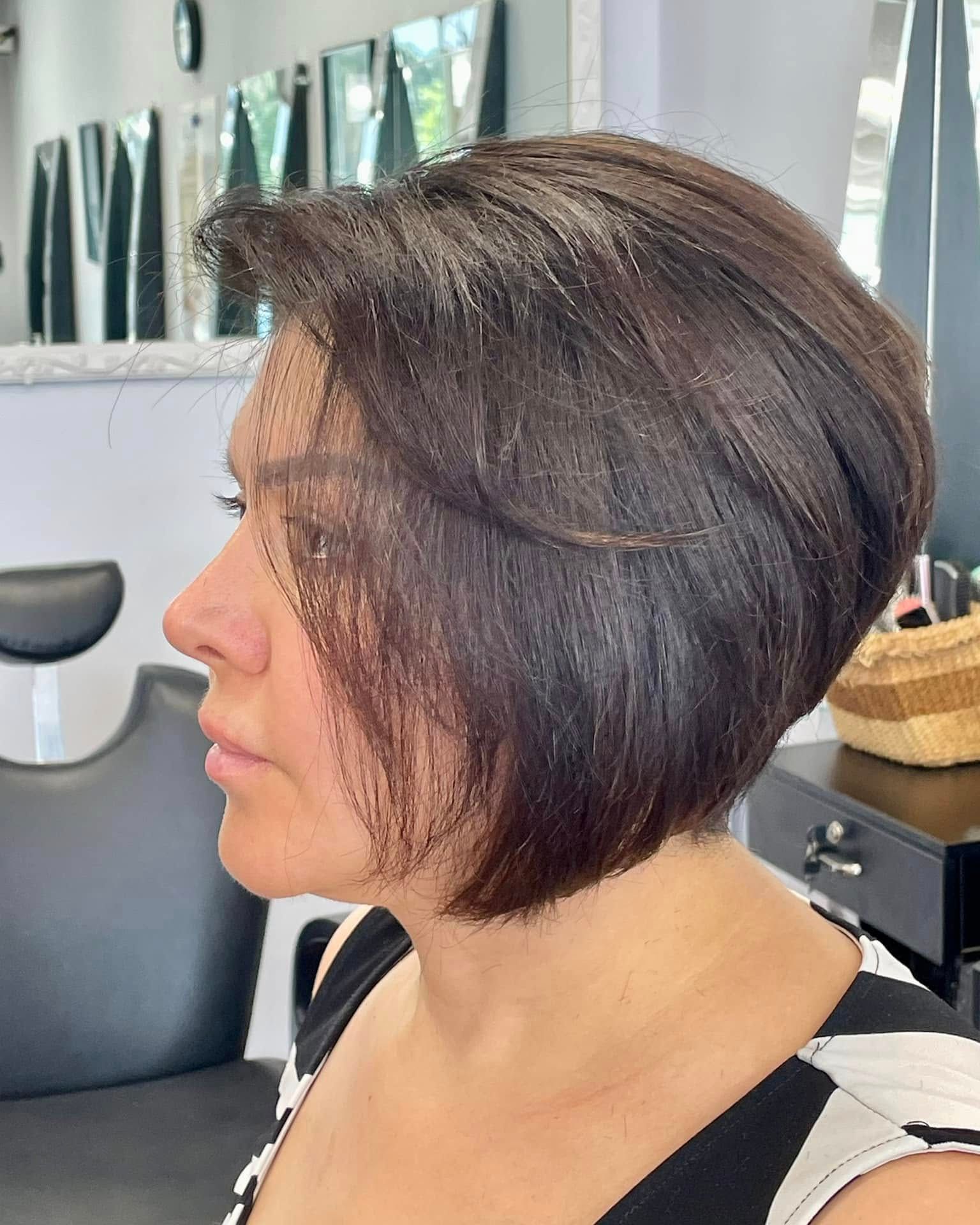 Woman with a short, dark brown bob haircut, looking left in a salon setting.