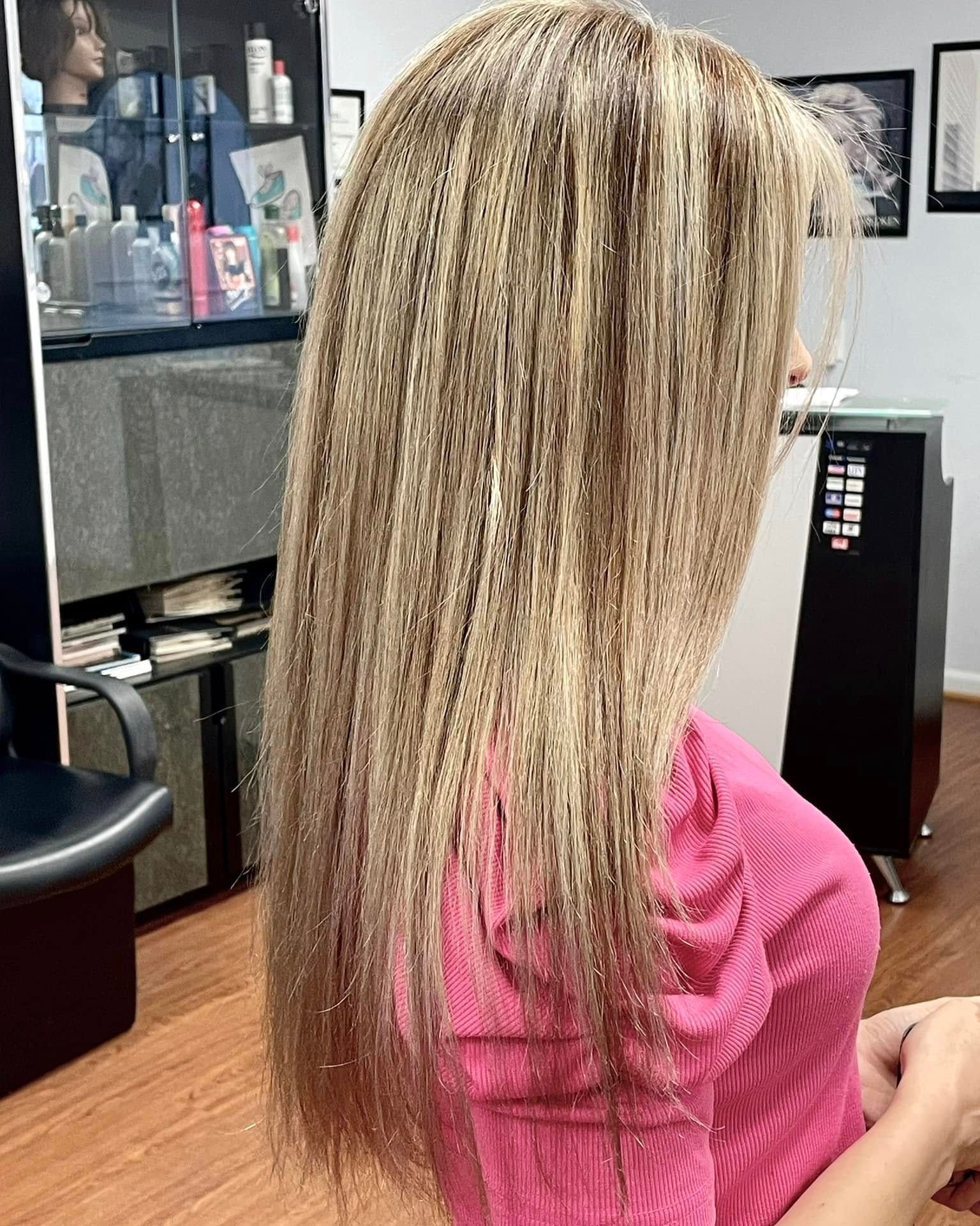 Woman with long, crimped blonde and brown hair, wearing a pink shirt, in a salon setting.