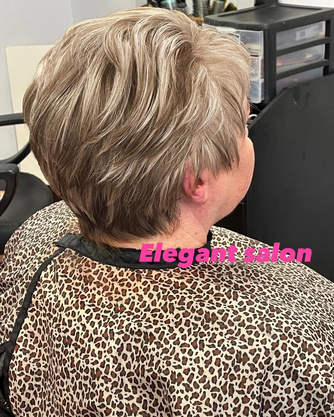 Woman with short, layered, ash-blonde hair at a salon, wearing a leopard-print cape. 