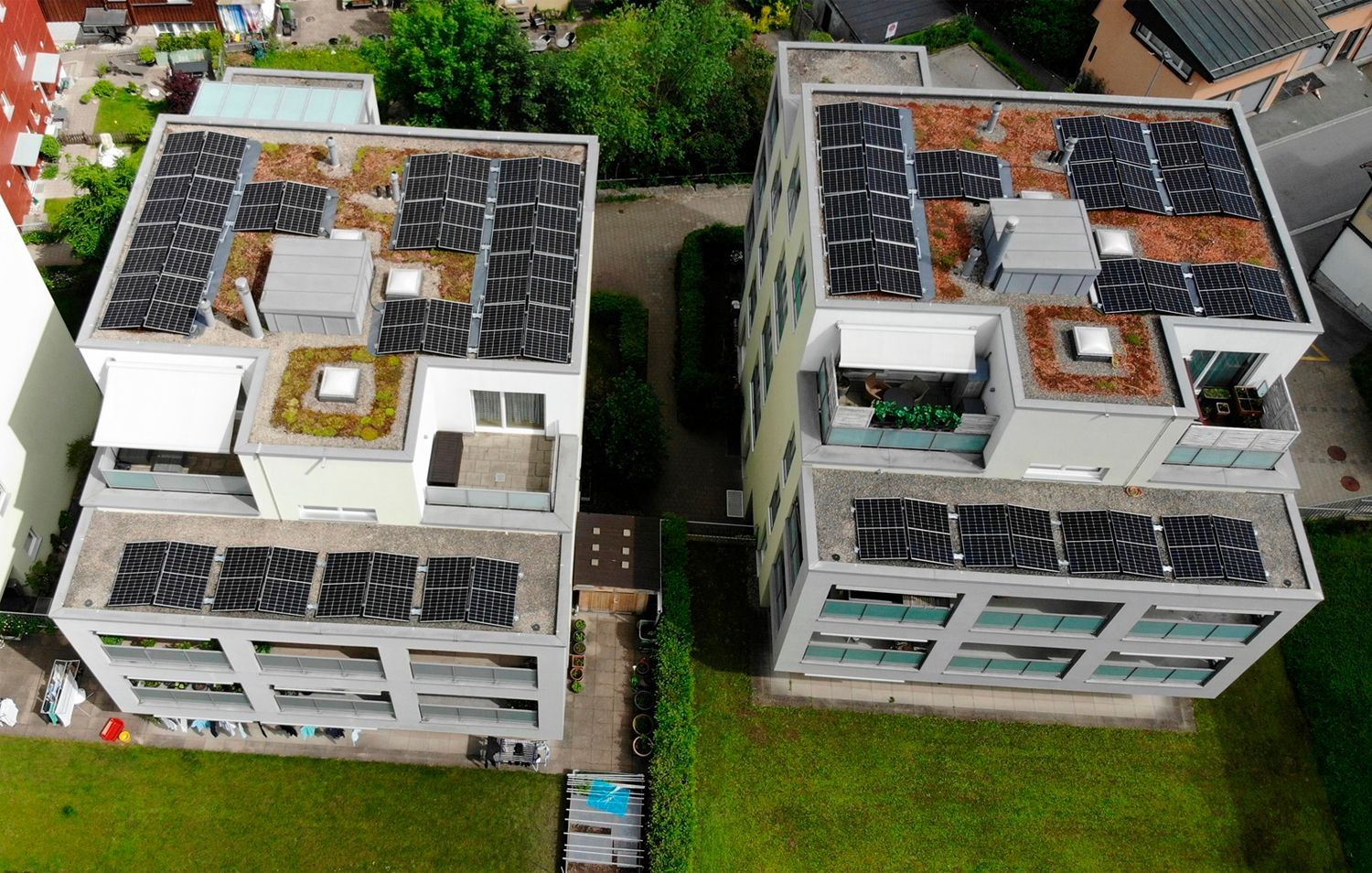 Zwei Mehrfamilienhäuser mit Solarmodulen und Gründächern, von oben gesehen.