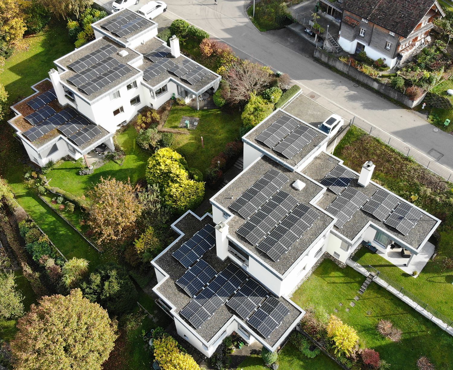 Luftaufnahme von weissen Häusern mit Solarmodulen auf den Dächern, umgeben von grünem Gras und Bäumen.