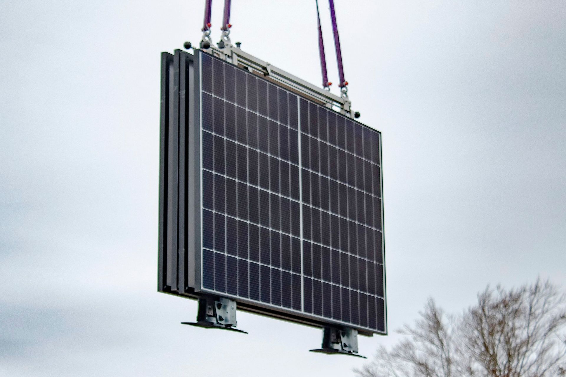 Solarpanel das an Krankabeln vor einem bewölkten Himmel aufgehängt ist.