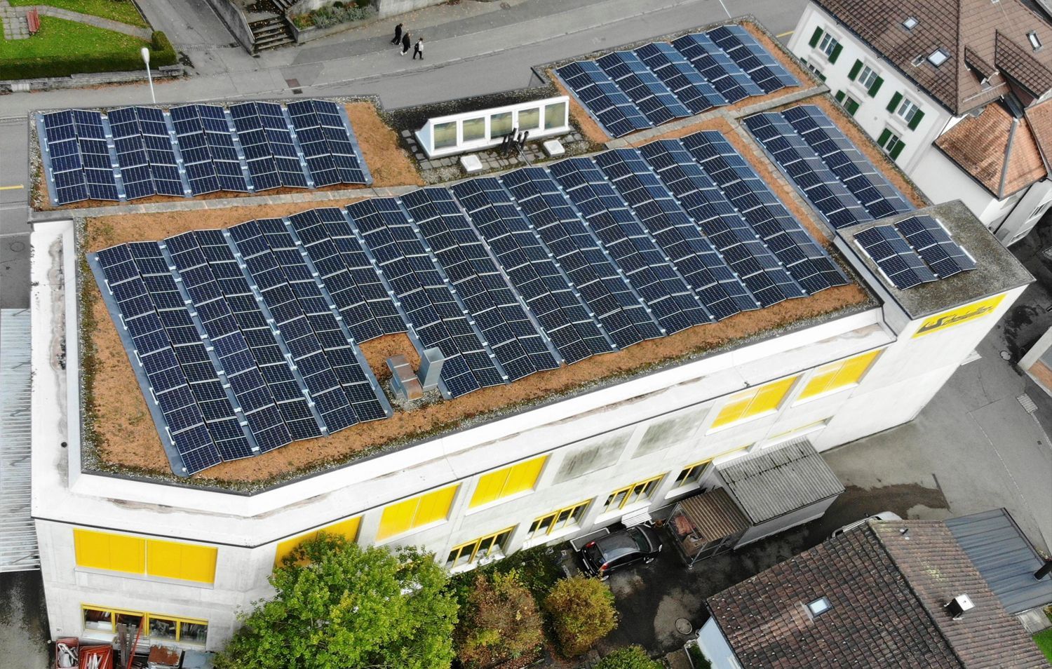 Solarmodule bedecken in einer Luftaufnahme das Dach eines Gebäudes. Gelbe Markisen, andere Gebäude umgeben es.