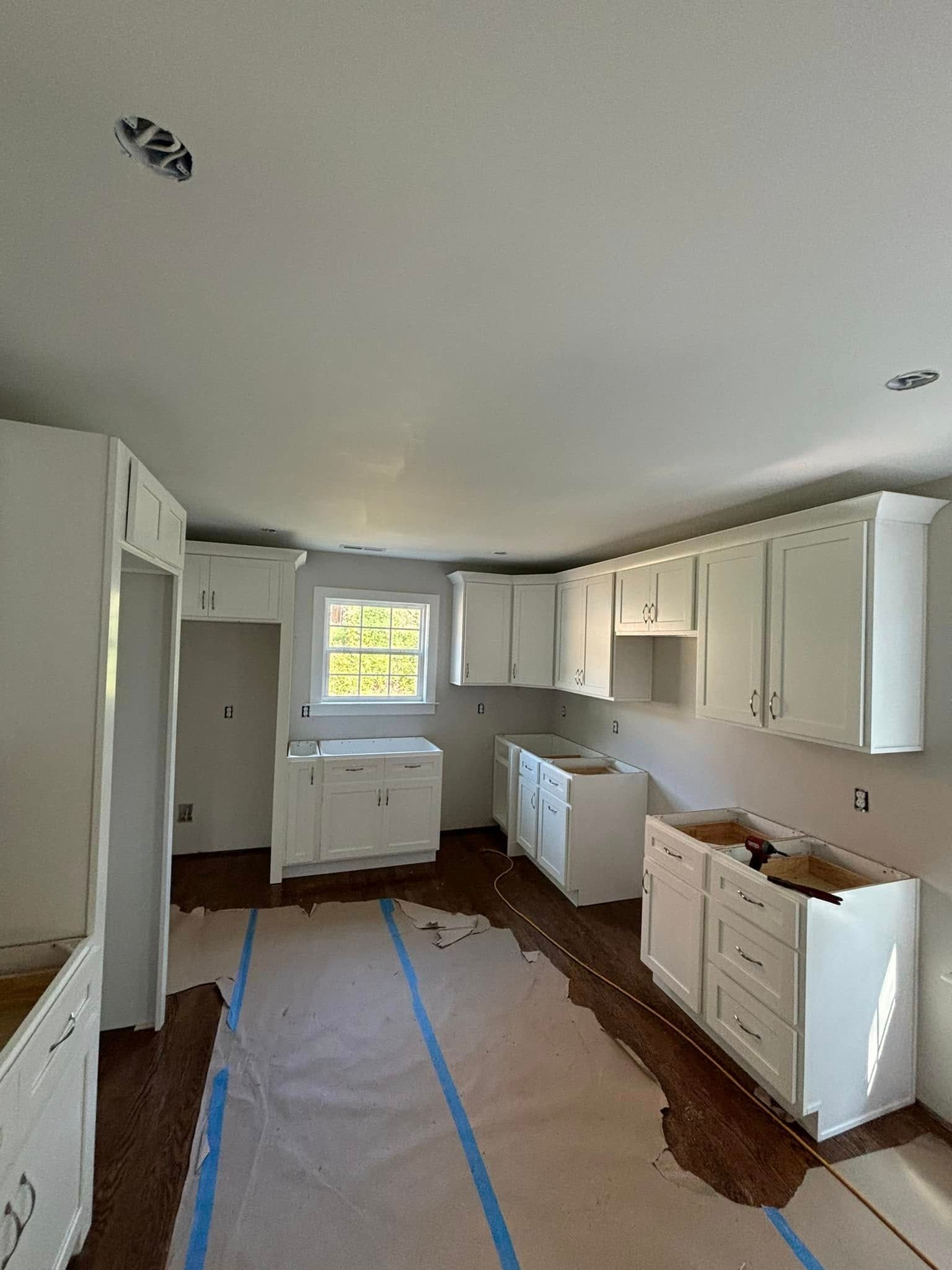 White kitchen cabinets in a room with a window, under construction.