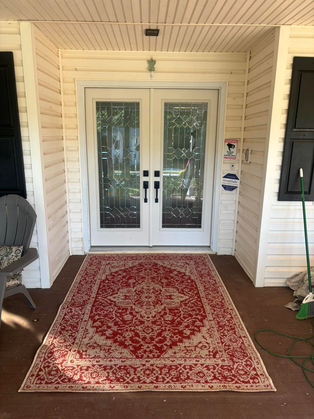 Red rug in front of white double doors on a porch with beige siding and black shutters.