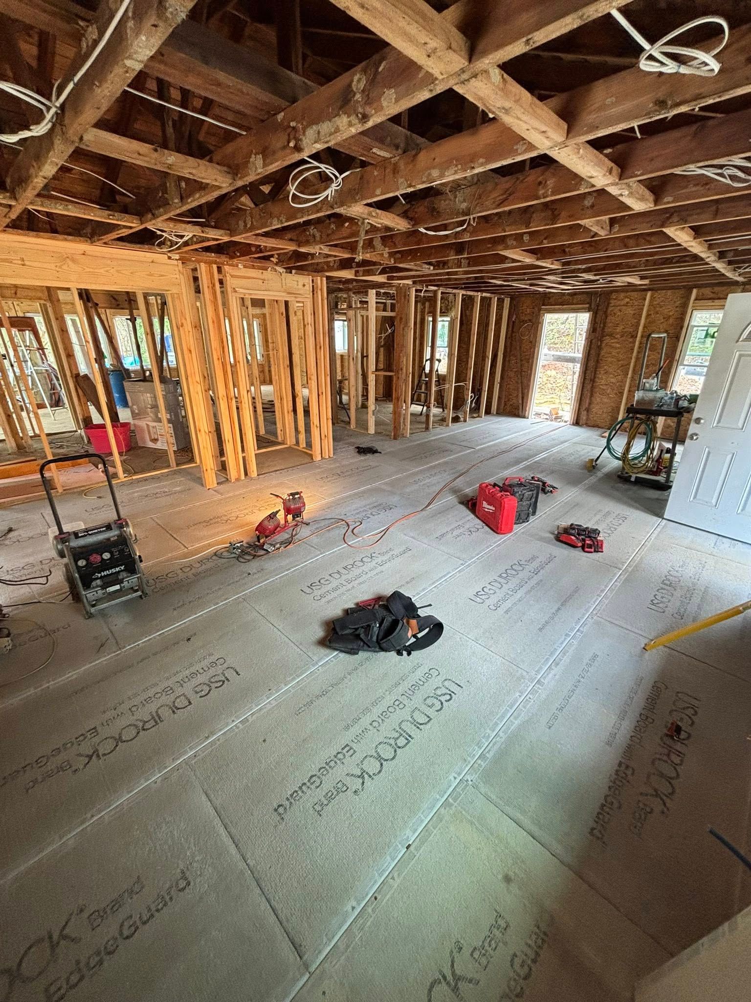 Interior view of a room under construction with exposed wooden beams, studs, and tools on the floor.