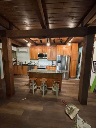 Rustic kitchen with wood beams, island with stools, and stainless steel appliances.