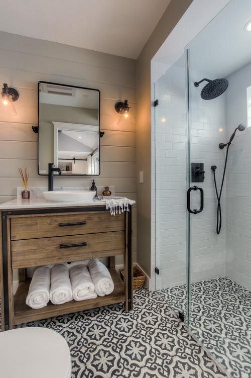 Bathroom with patterned floor, wooden vanity, glass shower, white subway tiles, and black fixtures.