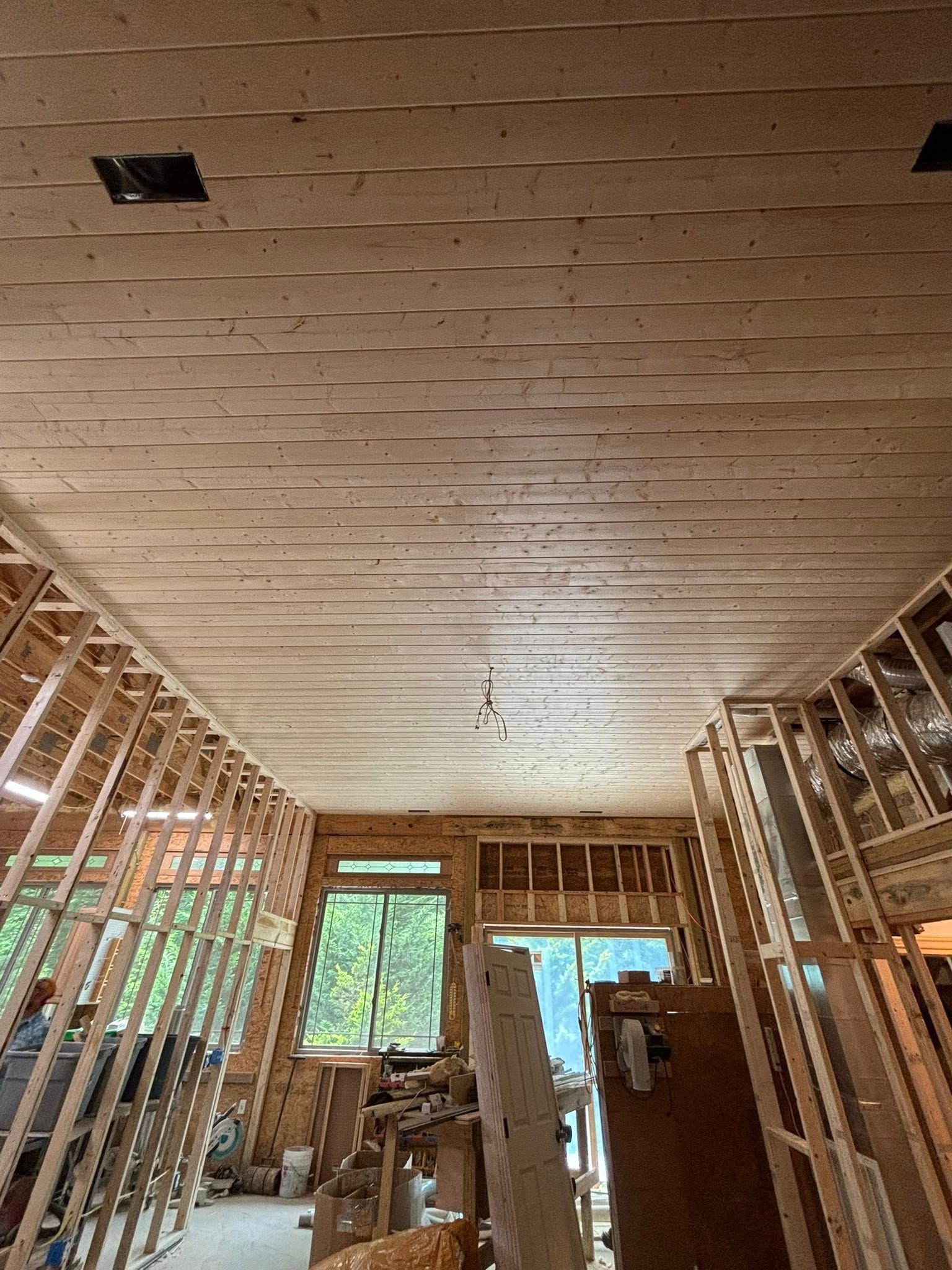 Interior view of a room under construction with wood-paneled ceiling and exposed wooden framing.