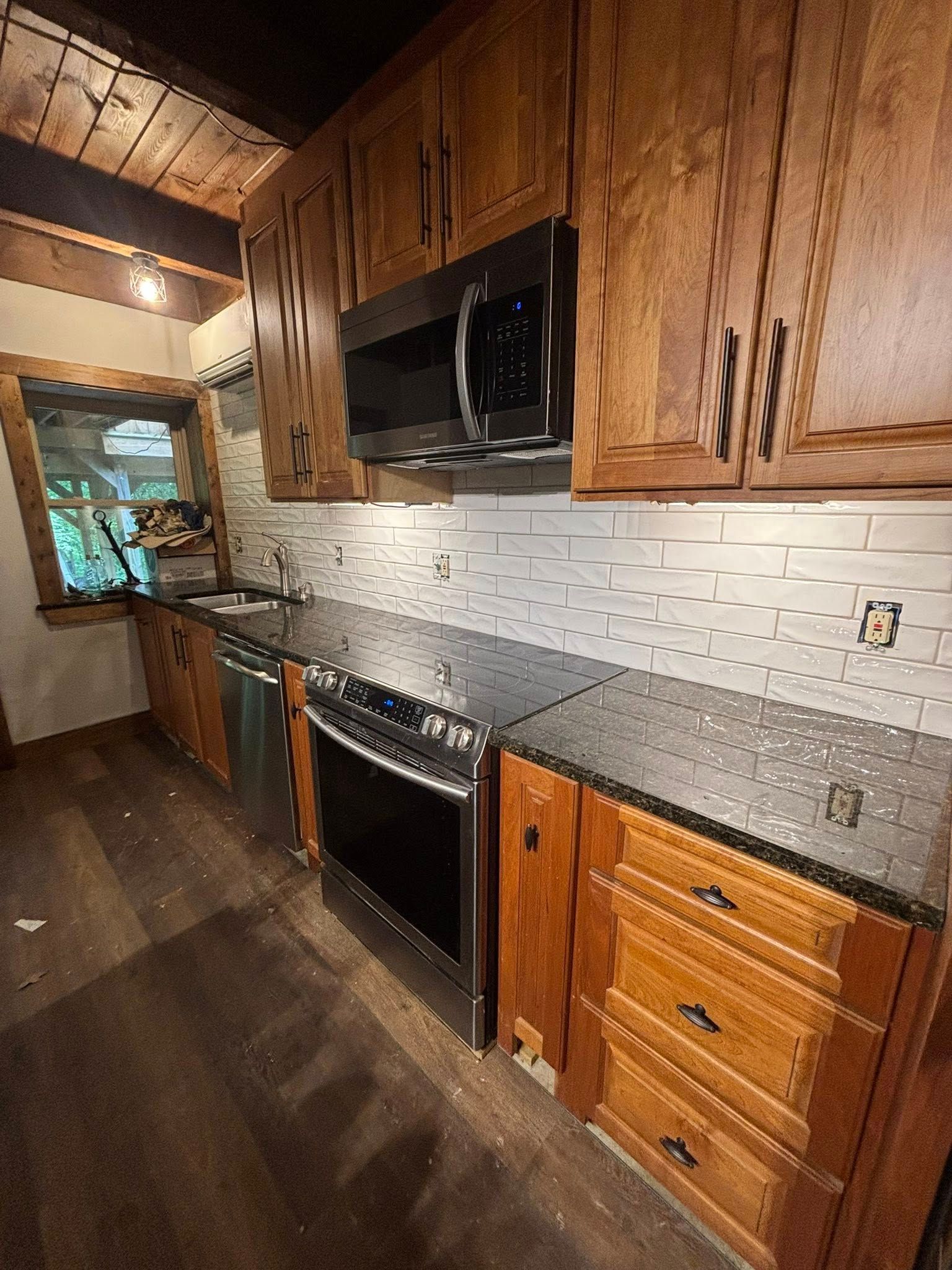 Kitchen with brown cabinets, stainless steel appliances, black countertop, and white tile backsplash.