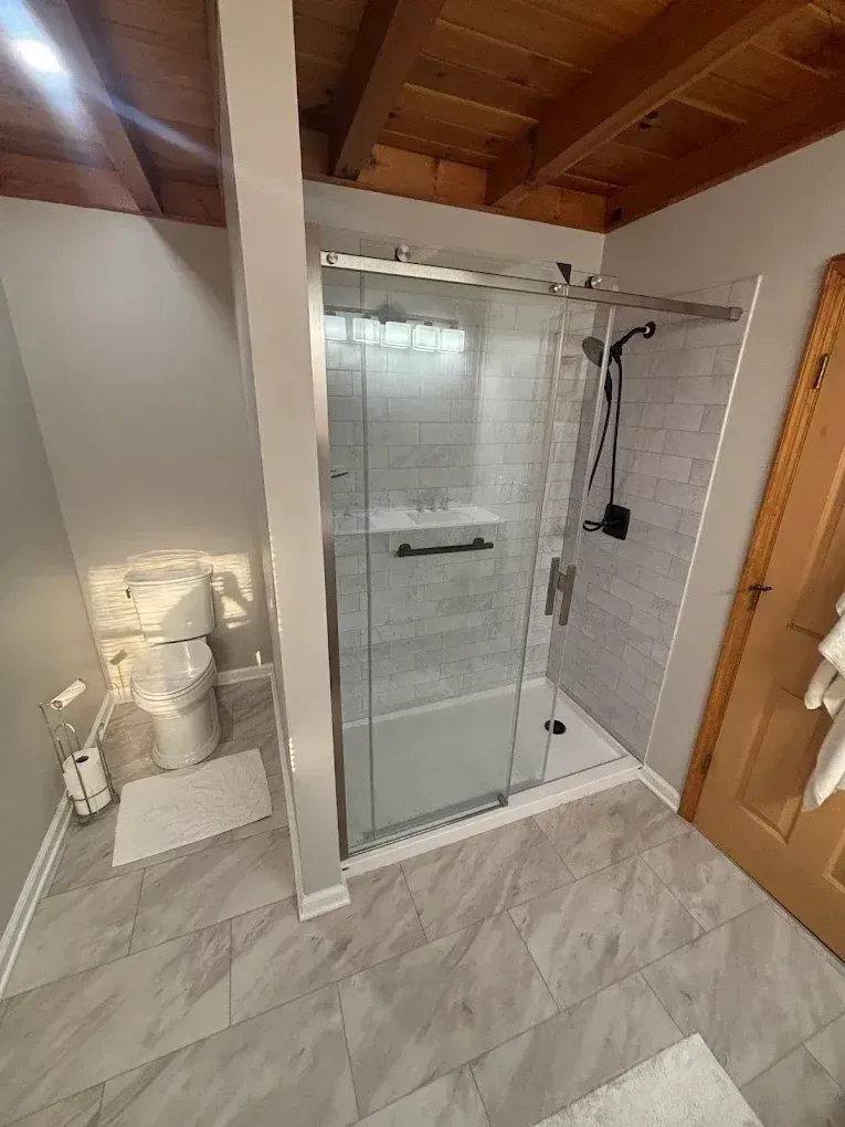 Modern bathroom with a glass shower, toilet, and wooden door.