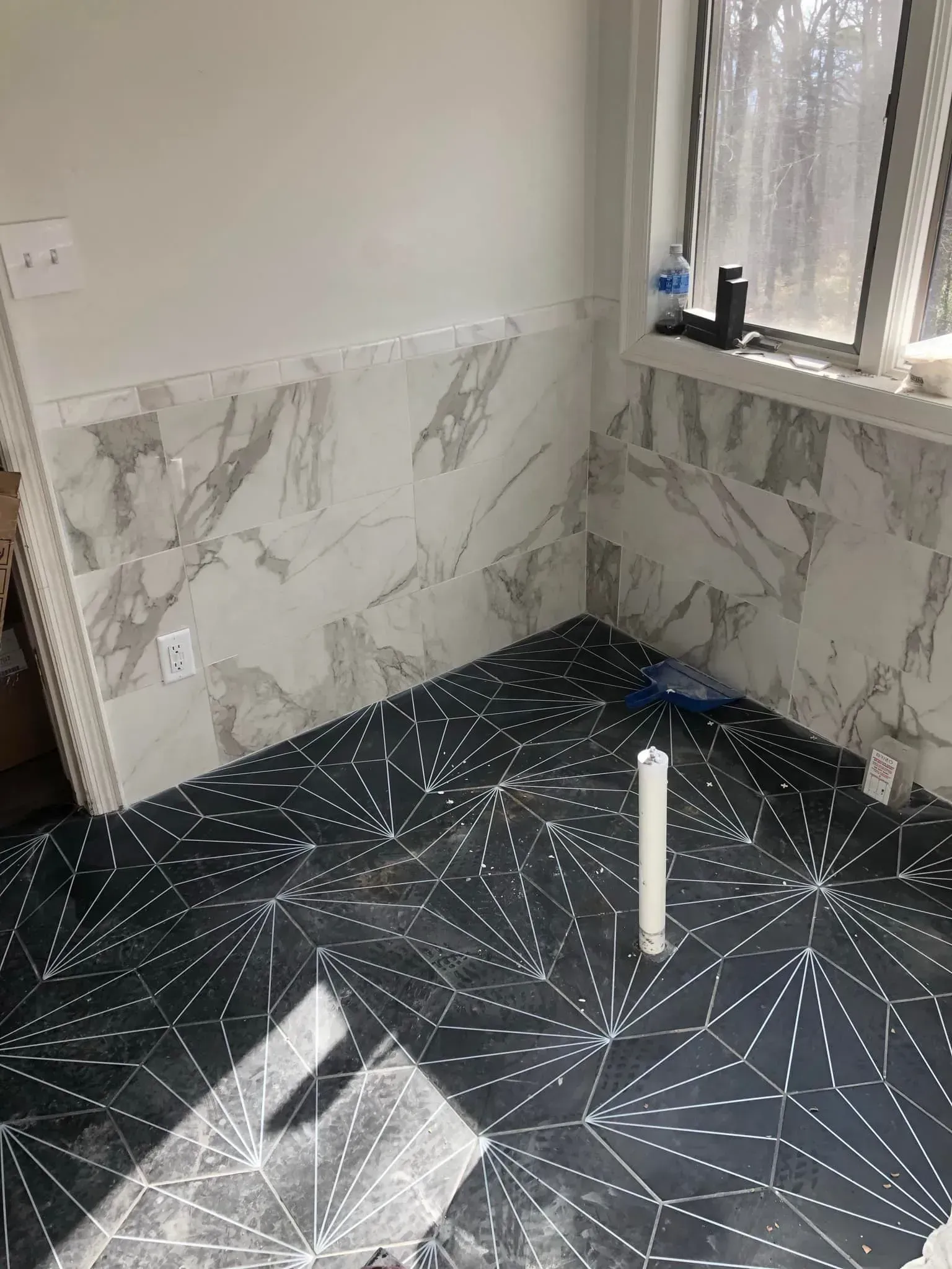 Bathroom with black patterned floor tiles, marble-look wall tiles, and a window.