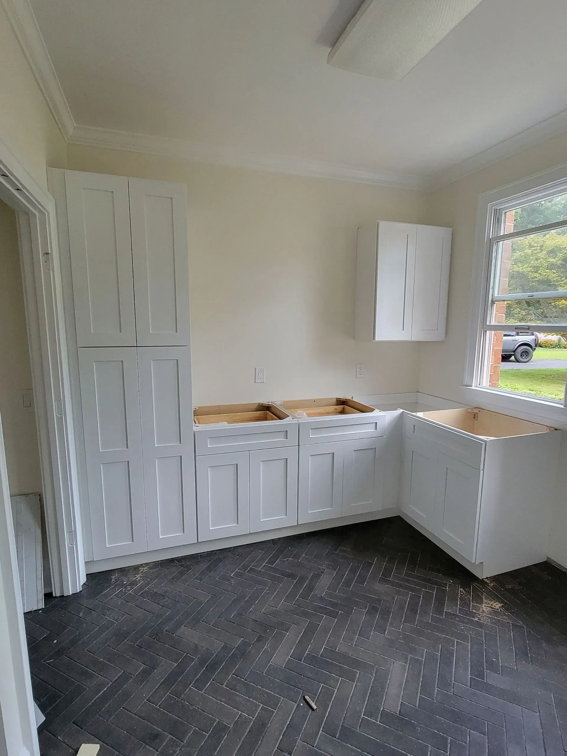 Kitchen cabinets, white, installed on beige wall, dark gray herringbone floor.
