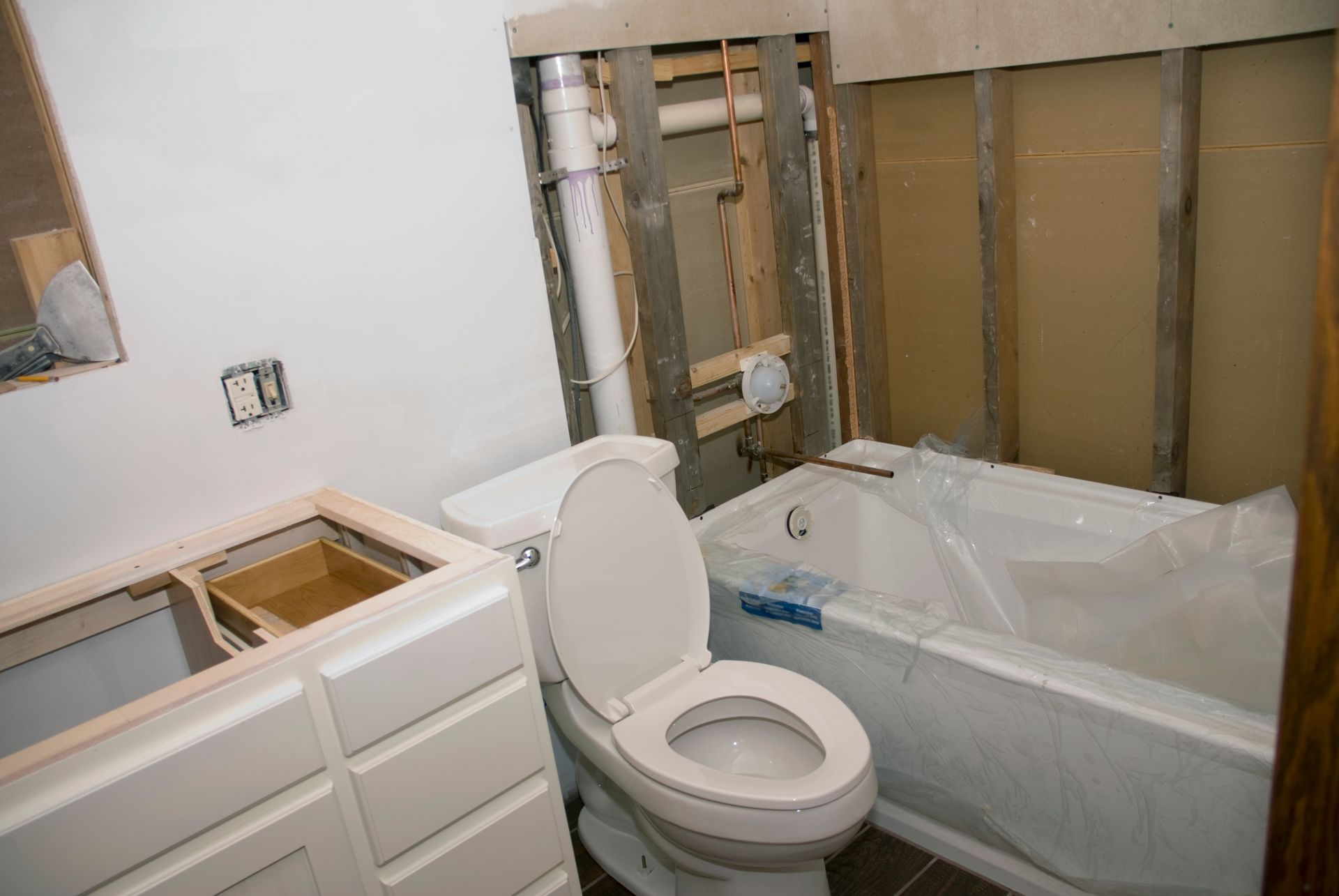 Bathroom under renovation with exposed wall studs, toilet, bathtub, and vanity.