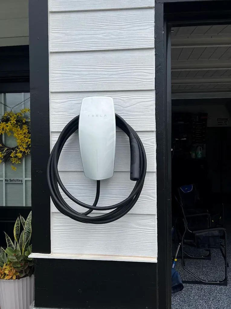 White EV charging station mounted on a house exterior with a coiled black cable.