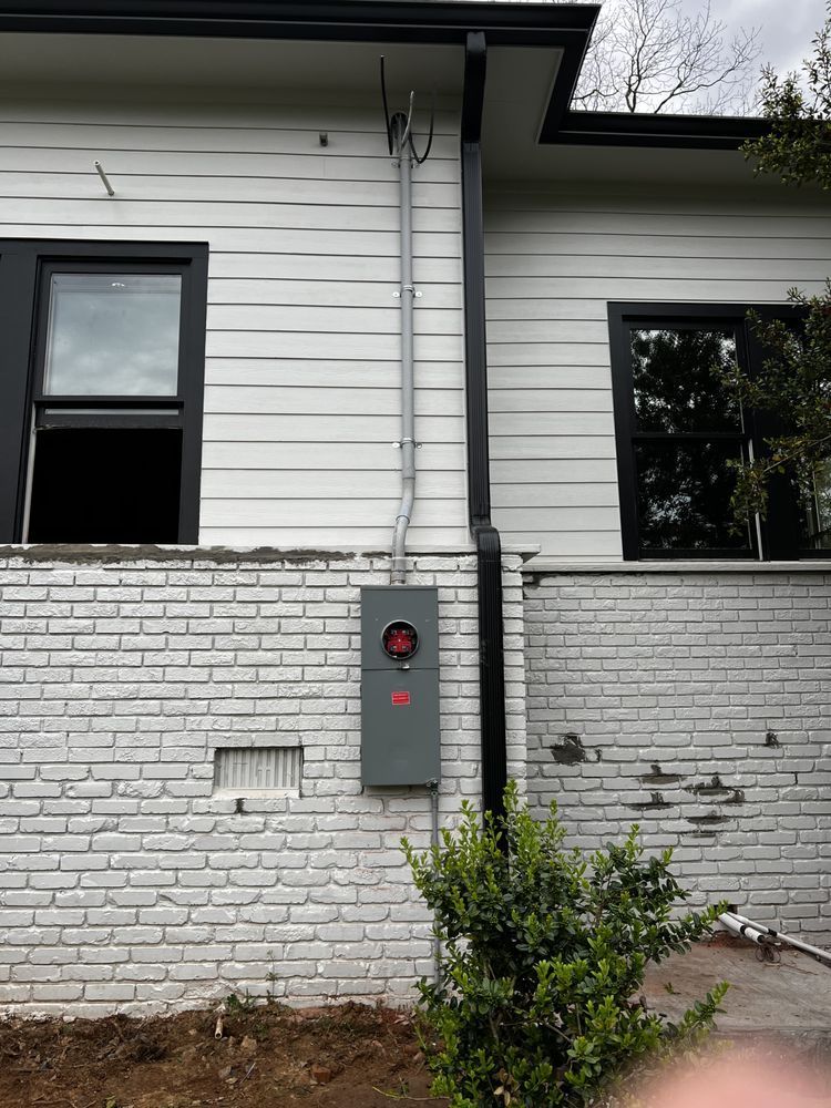 Exterior house wall with electrical meter box, white siding, brick lower wall, and small shrub under windows
