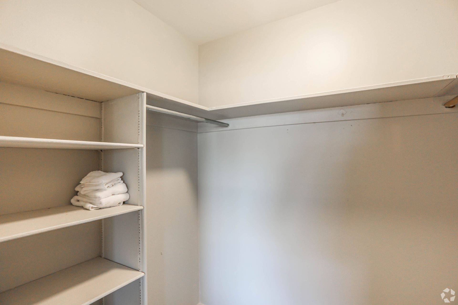 Empty walk-in closet with shelves on one side and a rod for hanging clothes.