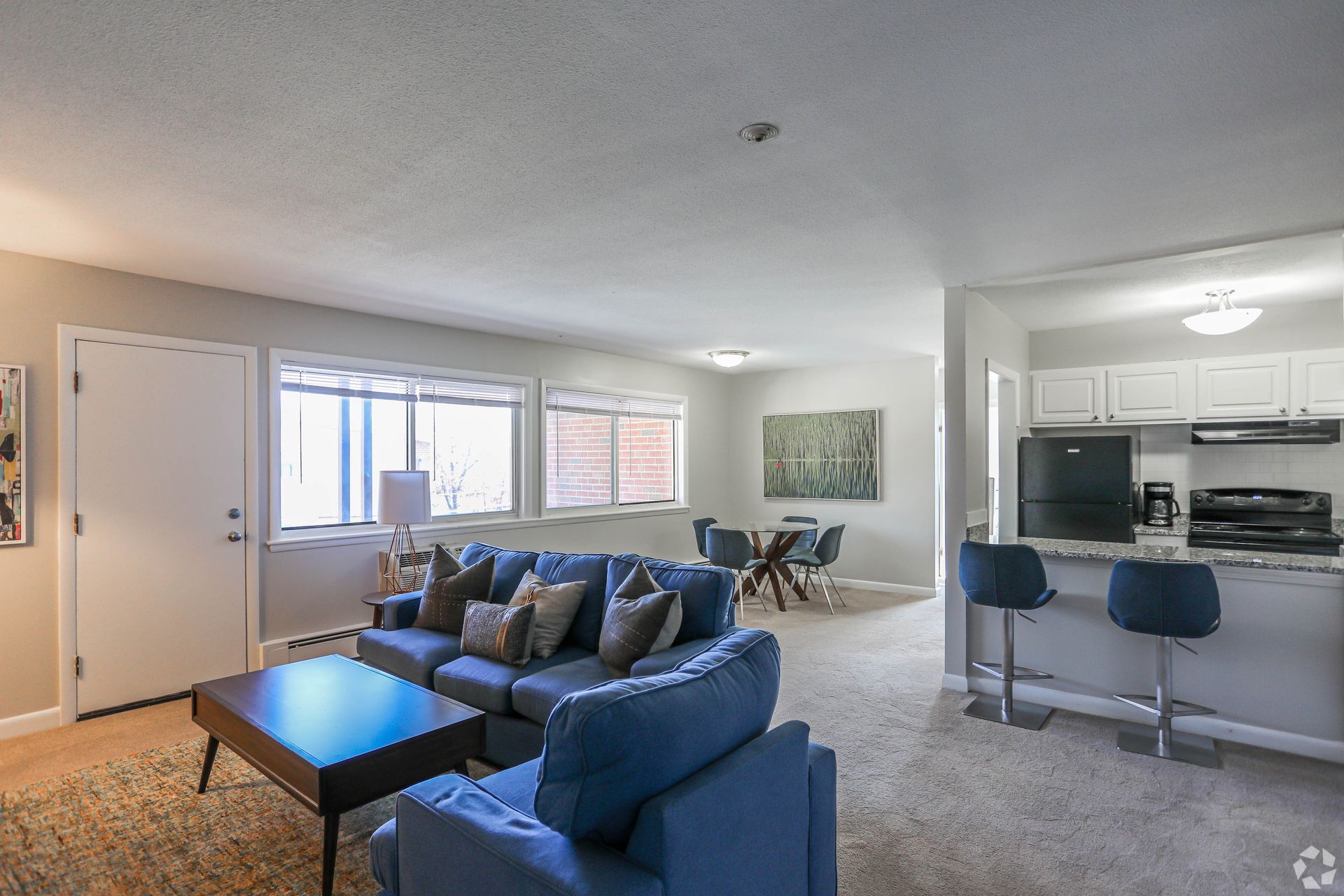 Open-concept living space with a blue sofa, dining table, and kitchen with bar seating.