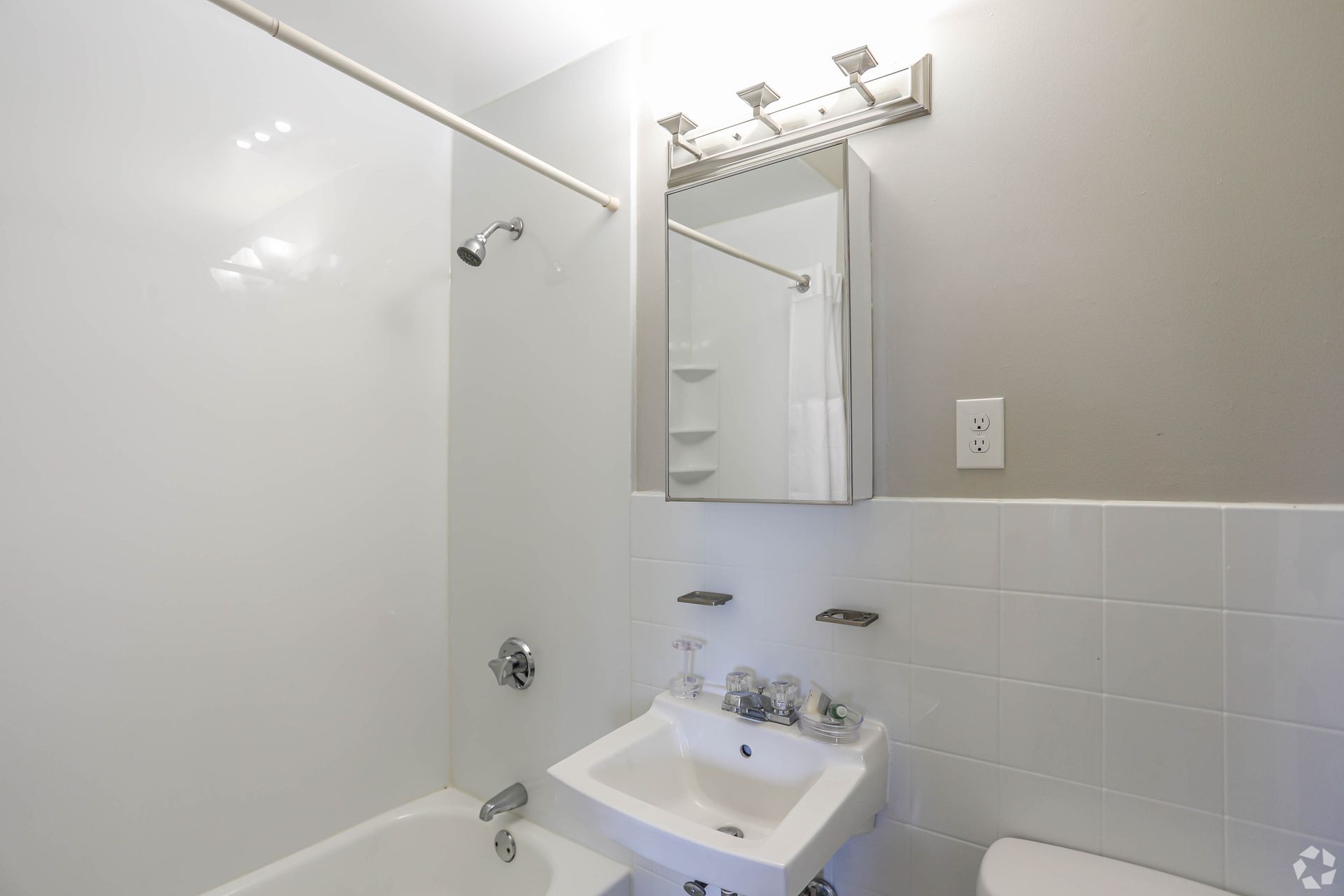 White bathroom with a shower, sink, mirror, and toilet.