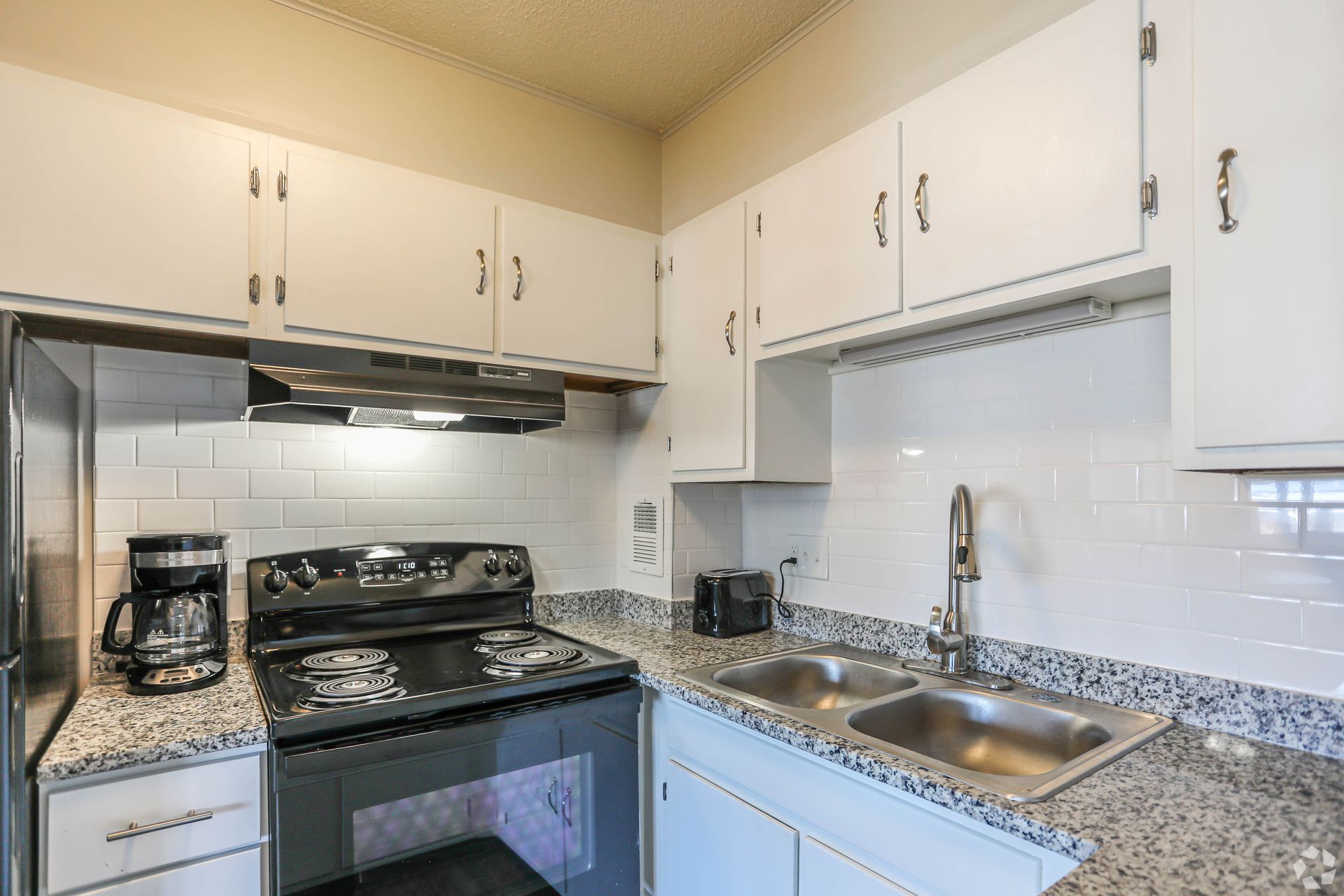 White kitchen with stove, sink, and cabinets; granite countertops.