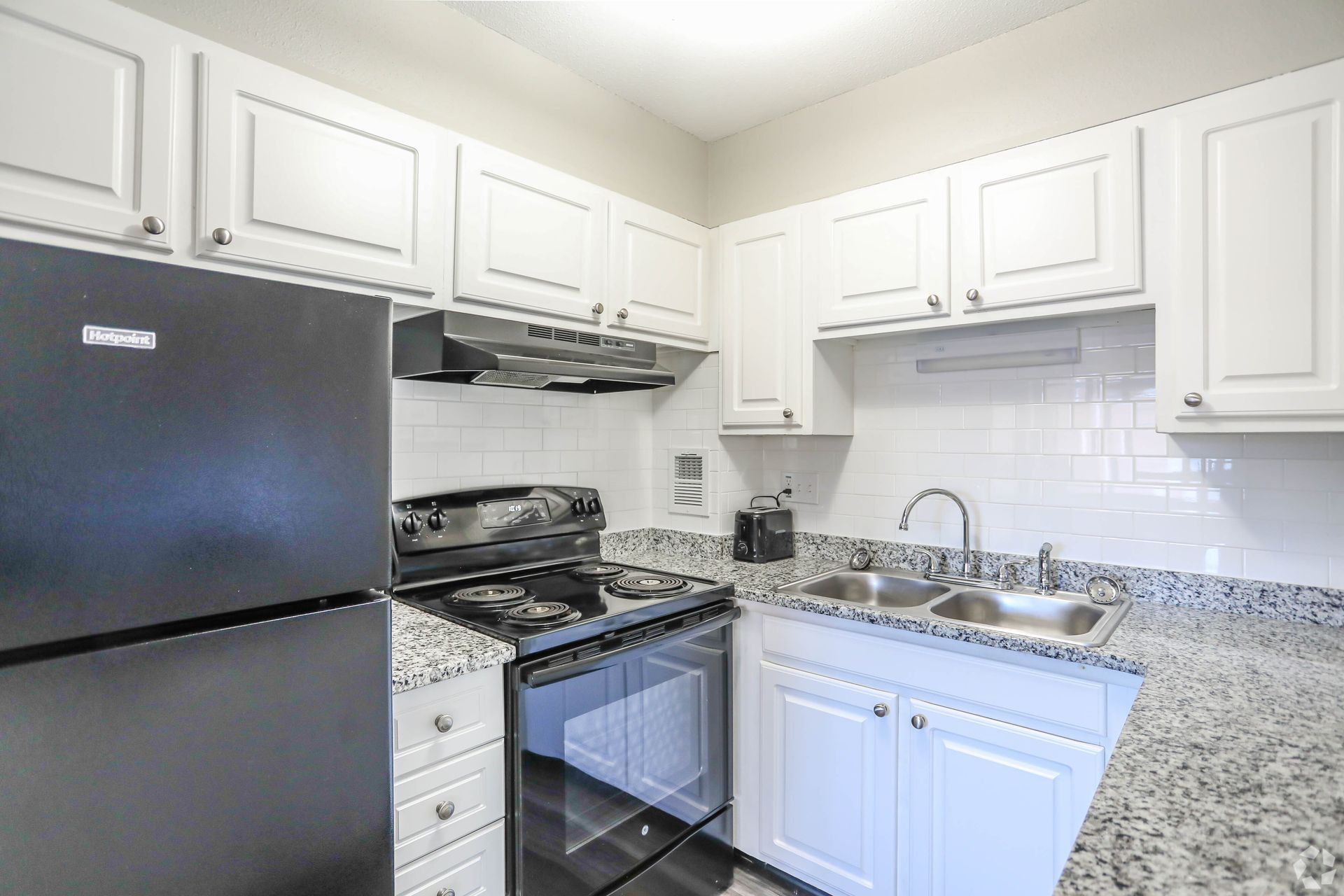 White kitchen with black appliances, granite countertops, and white cabinets.