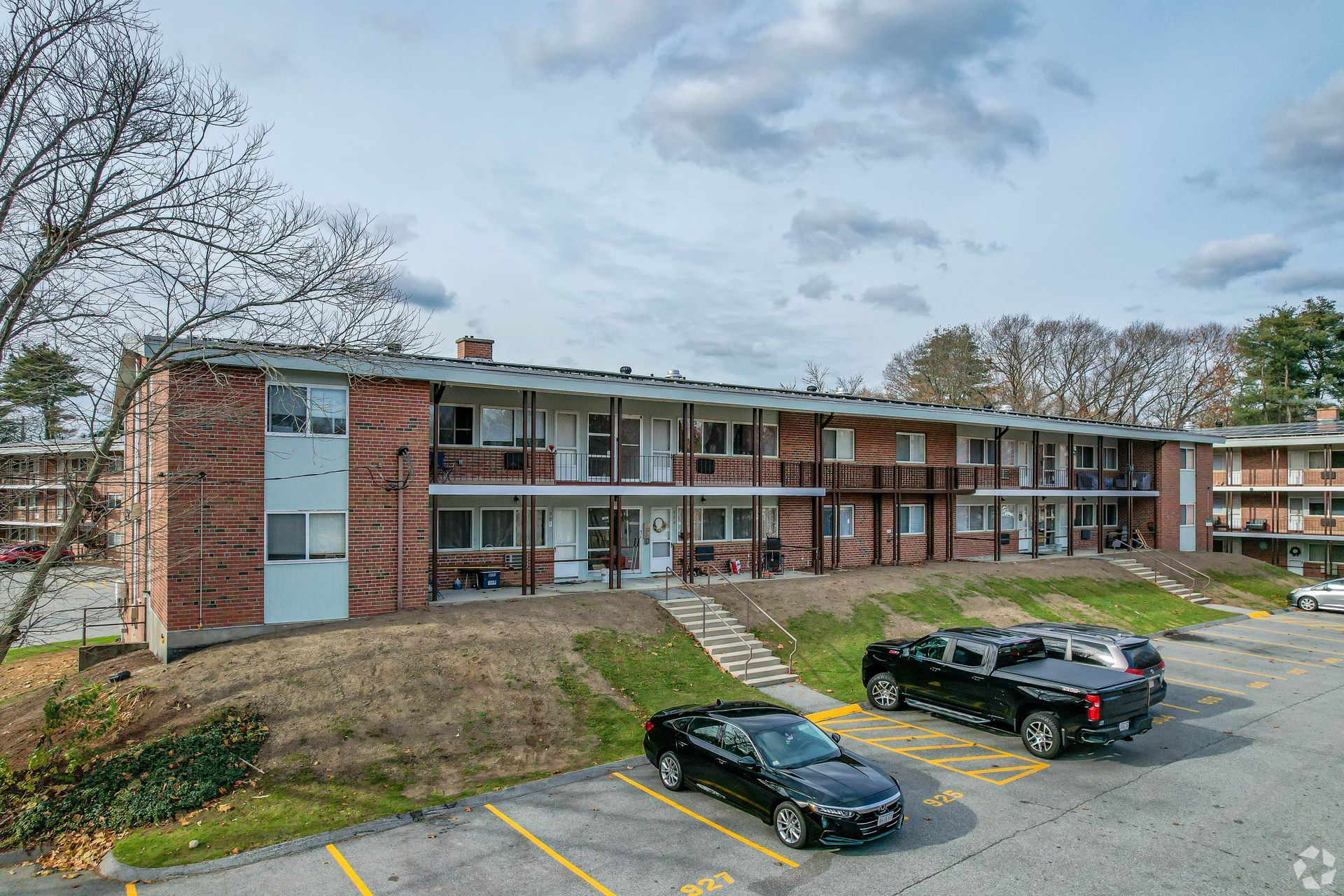 Apartment building with brick facade, two stories, small balconies, and a parking lot.