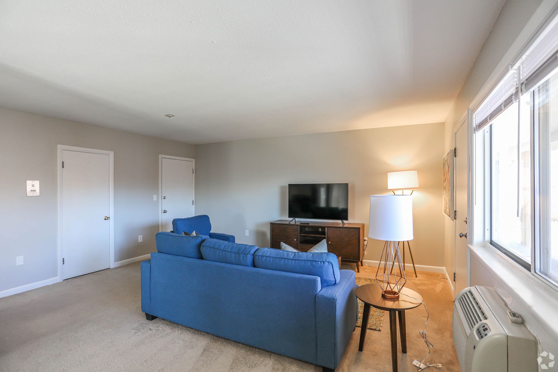 Living room with blue sofa, TV, and lamp near a window.