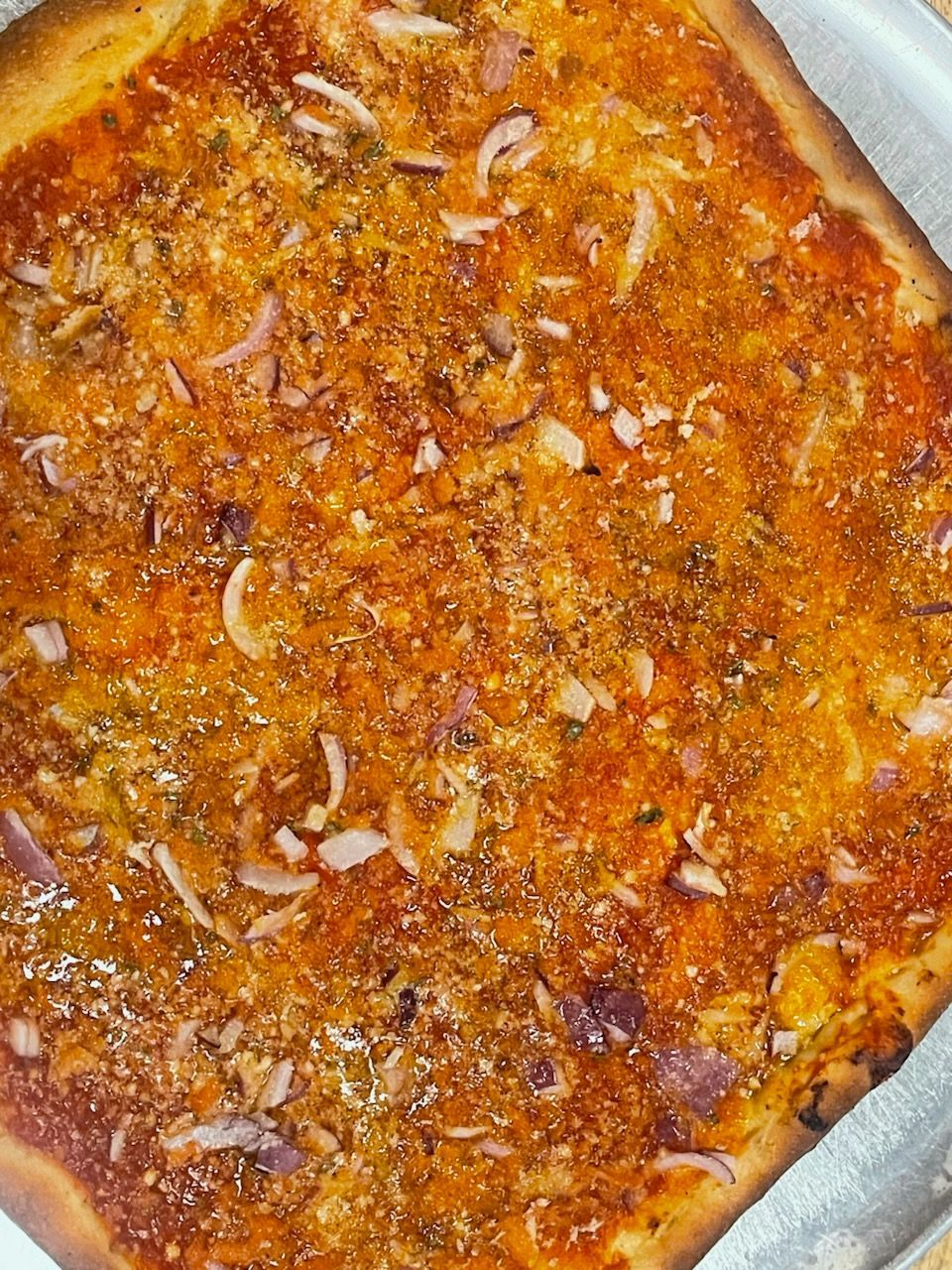 A close up of a pizza with tomato sauce and onions on a pan.