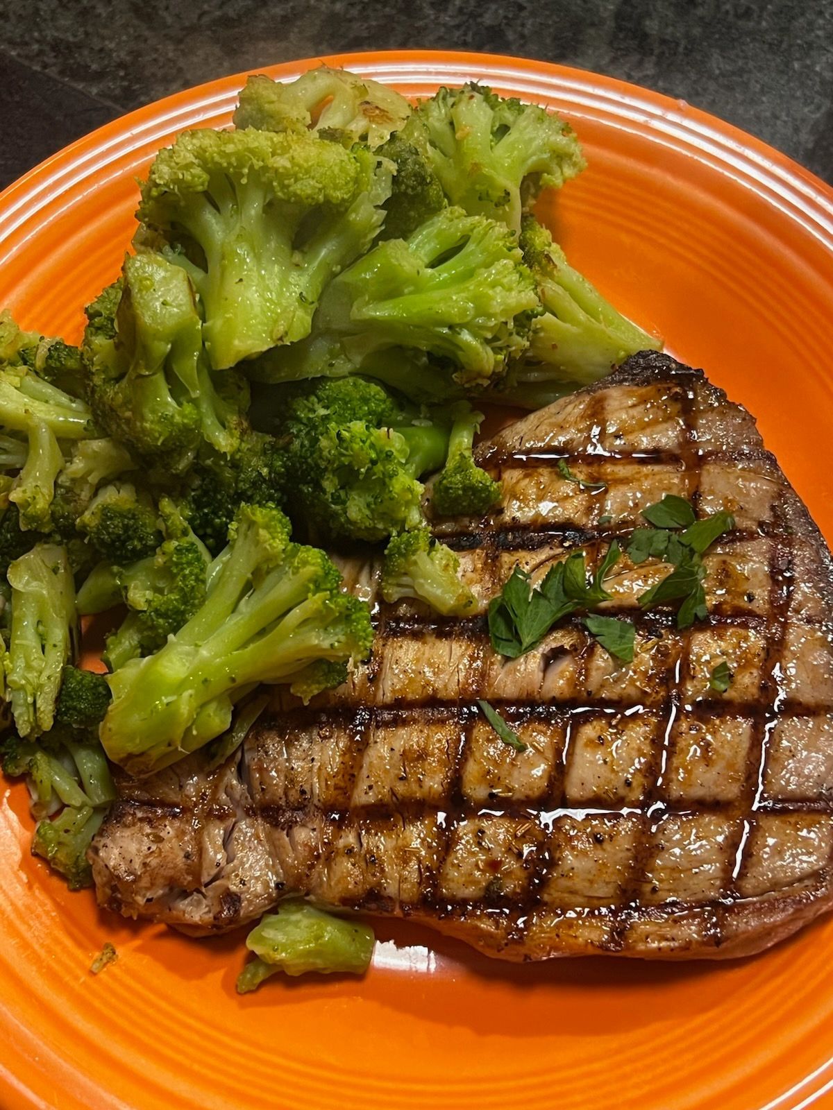 An orange plate topped with a steak and broccoli.
