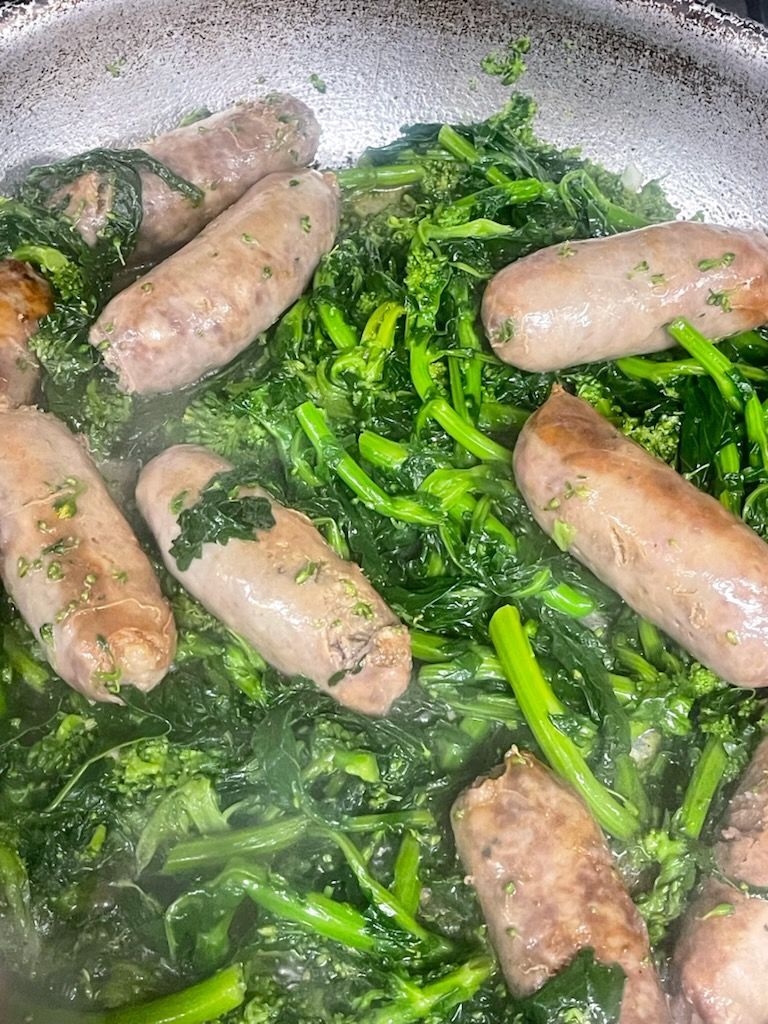 Sausages and spinach are being cooked in a pan.