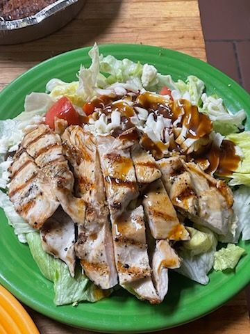 A green plate topped with grilled chicken and lettuce on a wooden table.