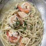 A close up of a bowl of noodles with shrimp in a sauce.