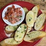 A red plate topped with garlic bread and a bowl of salsa.
