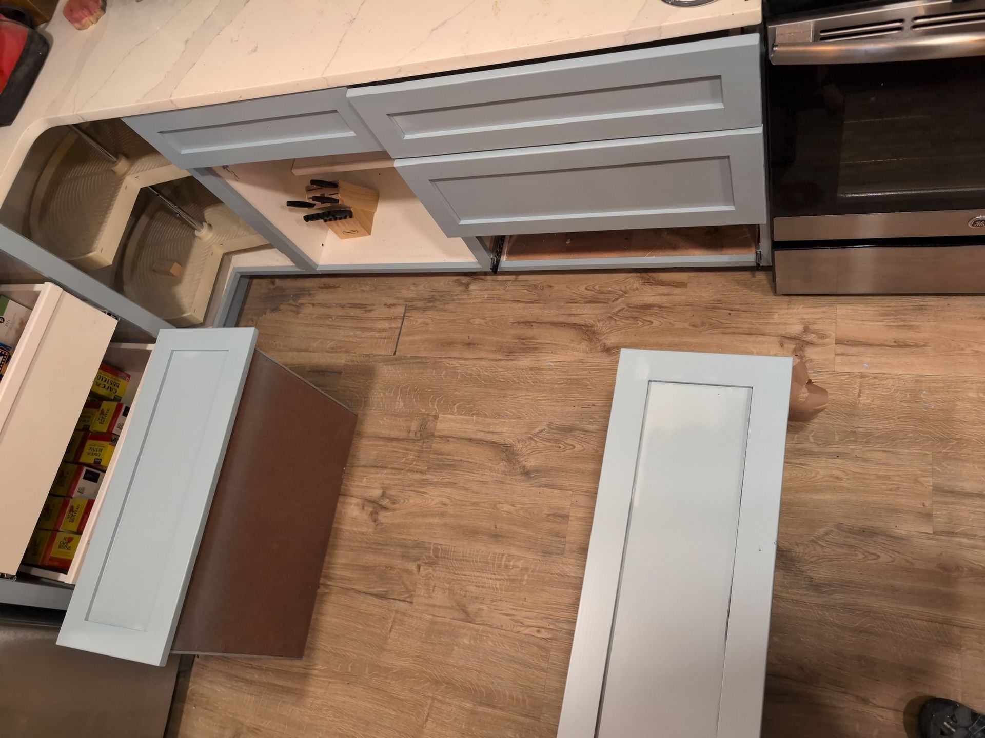 Light blue kitchen cabinets, drawers open, on a wood floor. A stainless steel stove is on the right.