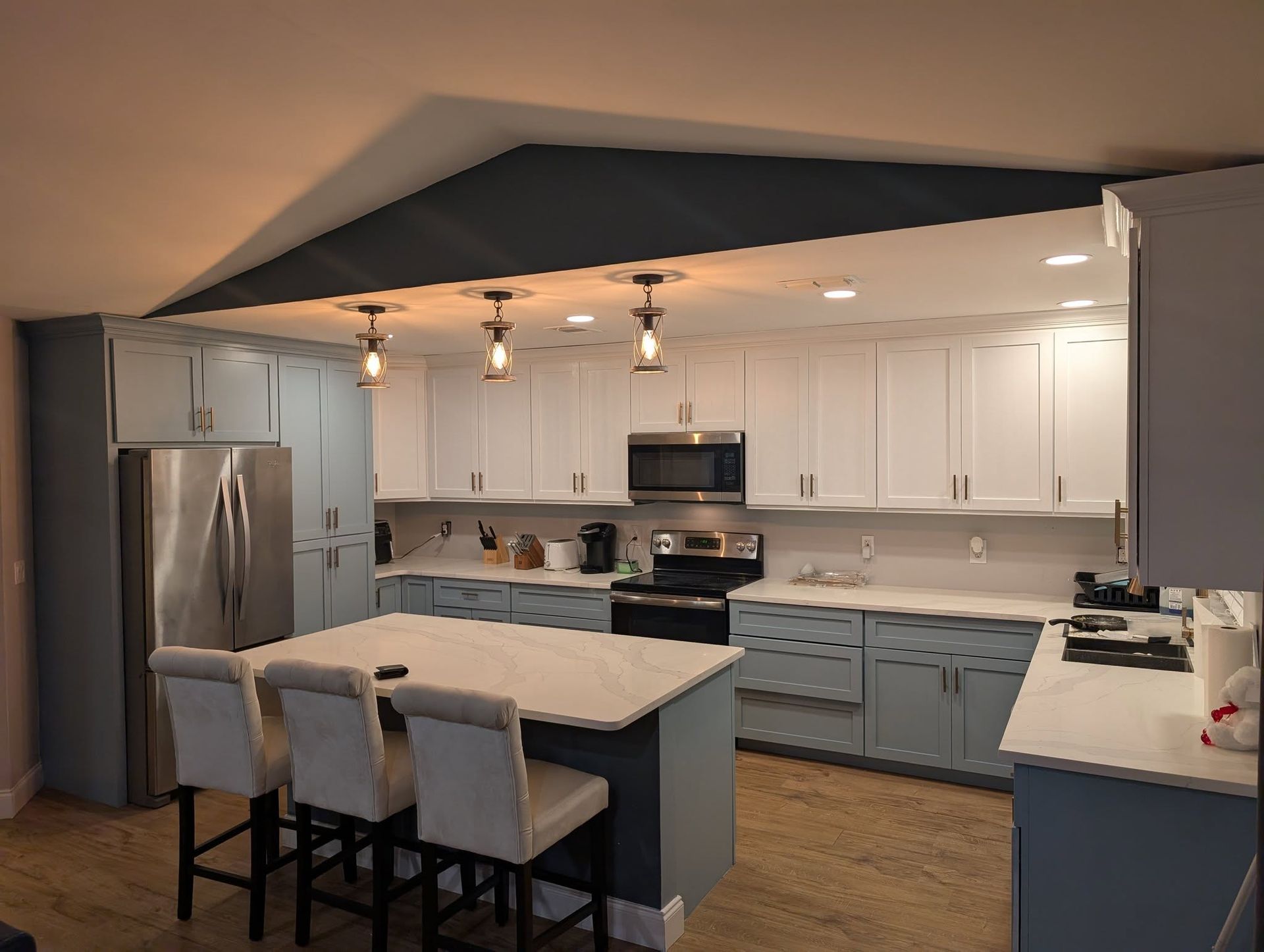 Modern kitchen with blue and white cabinets, stainless steel appliances, and an island with stools.