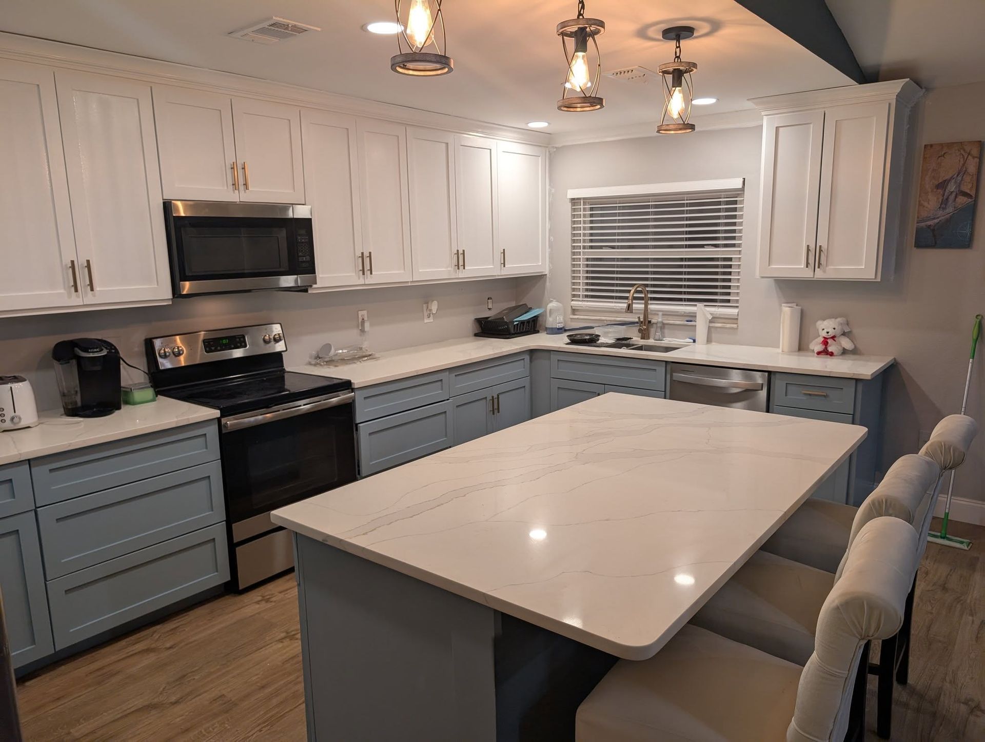 A modern kitchen with white and blue cabinets, a white countertop island, and stainless steel appliances.