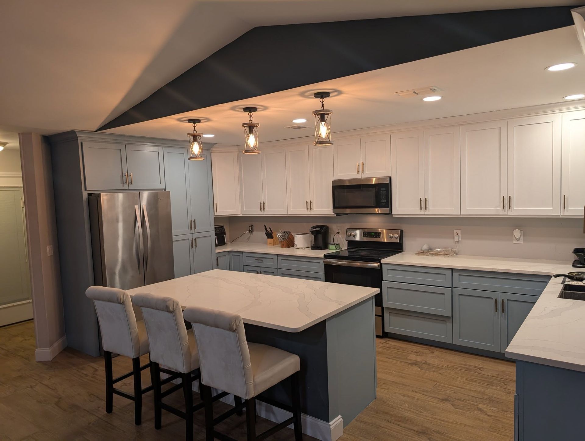 Modern kitchen with white and blue cabinets, island with seating, and stainless steel appliances.