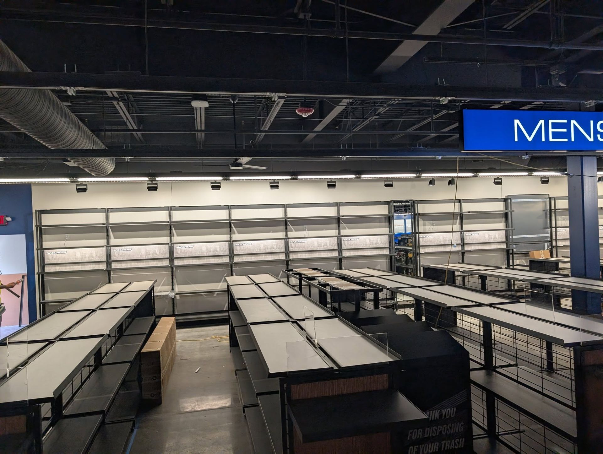 Empty men's clothing store with shelves and tables, under blue 