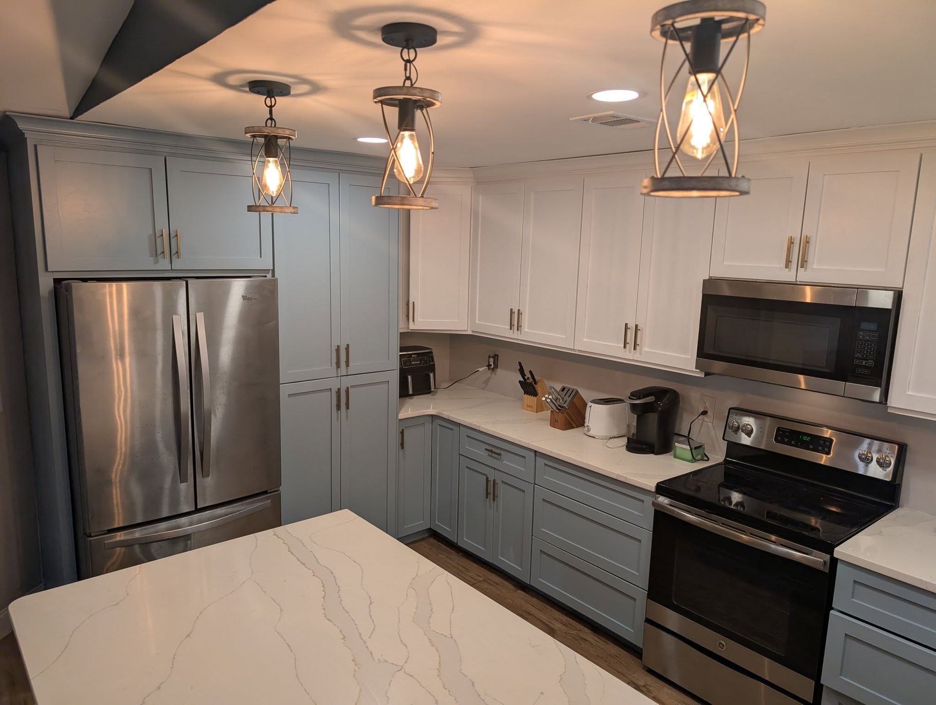 Kitchen with white and blue cabinets, stainless steel appliances, and pendant lights.