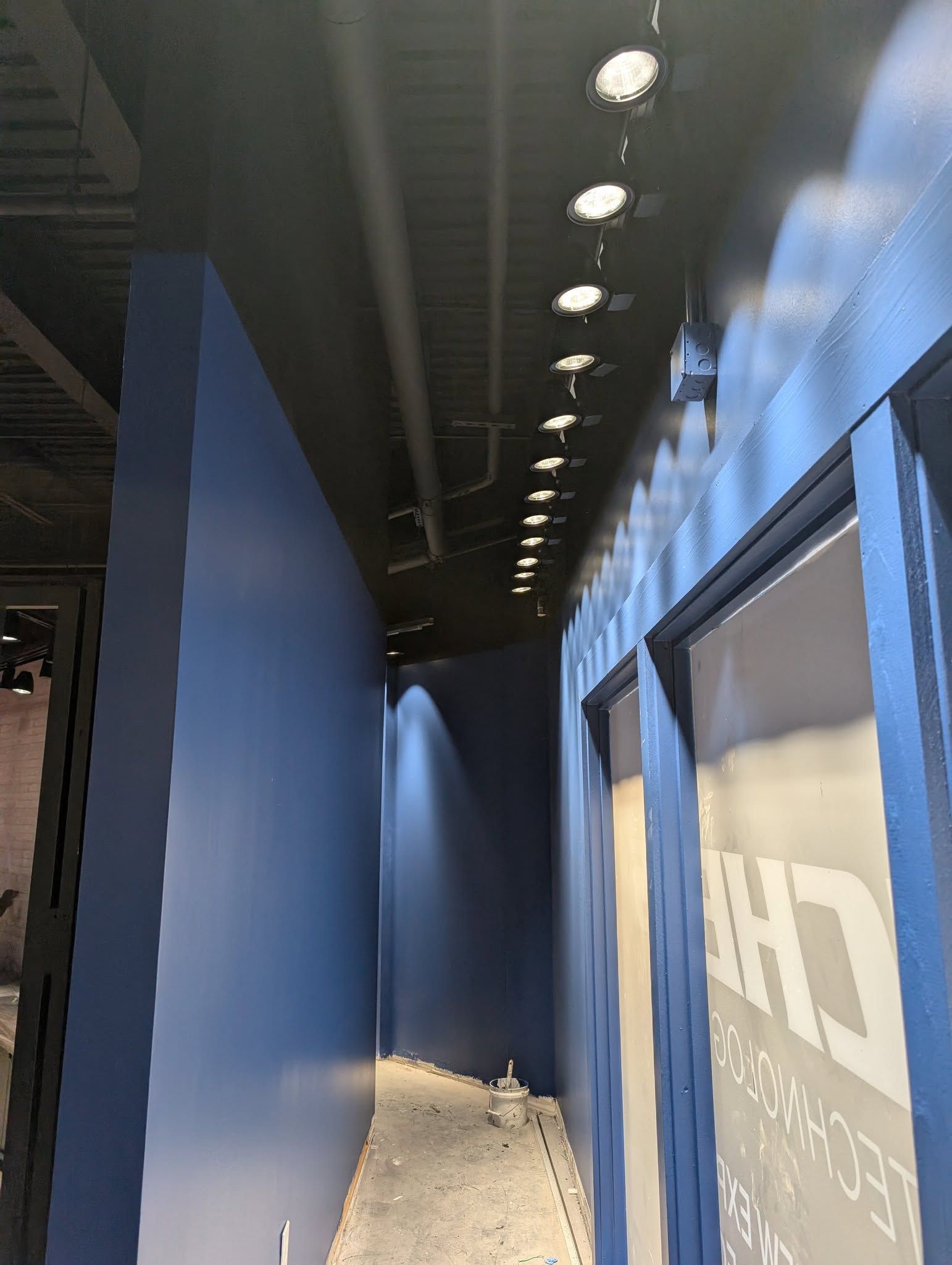 Narrow hallway with blue walls, black ceiling, recessed lighting, and a doorway on the right.